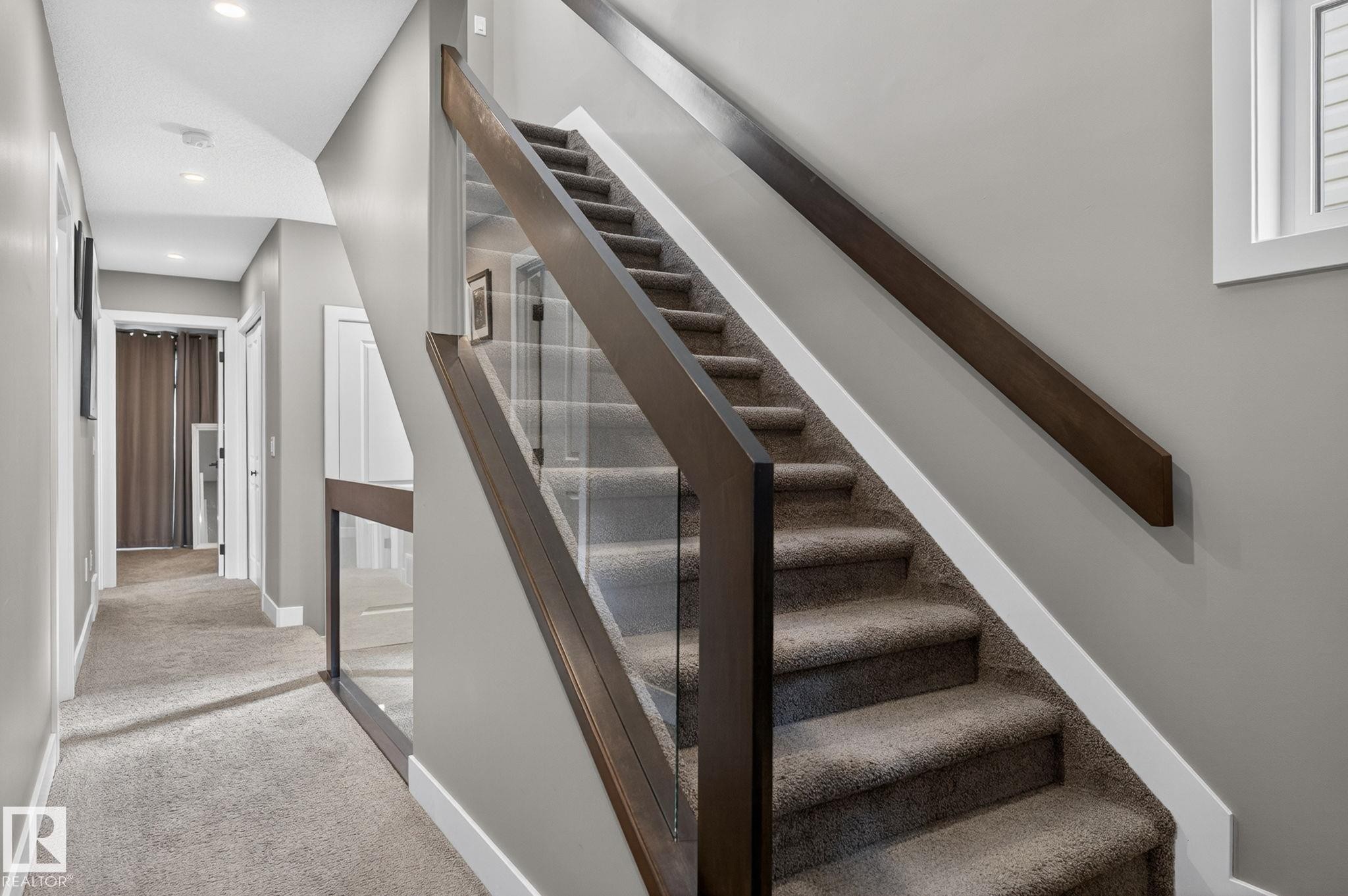 Contemporary staircase featuring glass railing and dark wood-finish handrails - 8809 148 Street, Edmonton, AB - Indoor Photo Showing Other Room