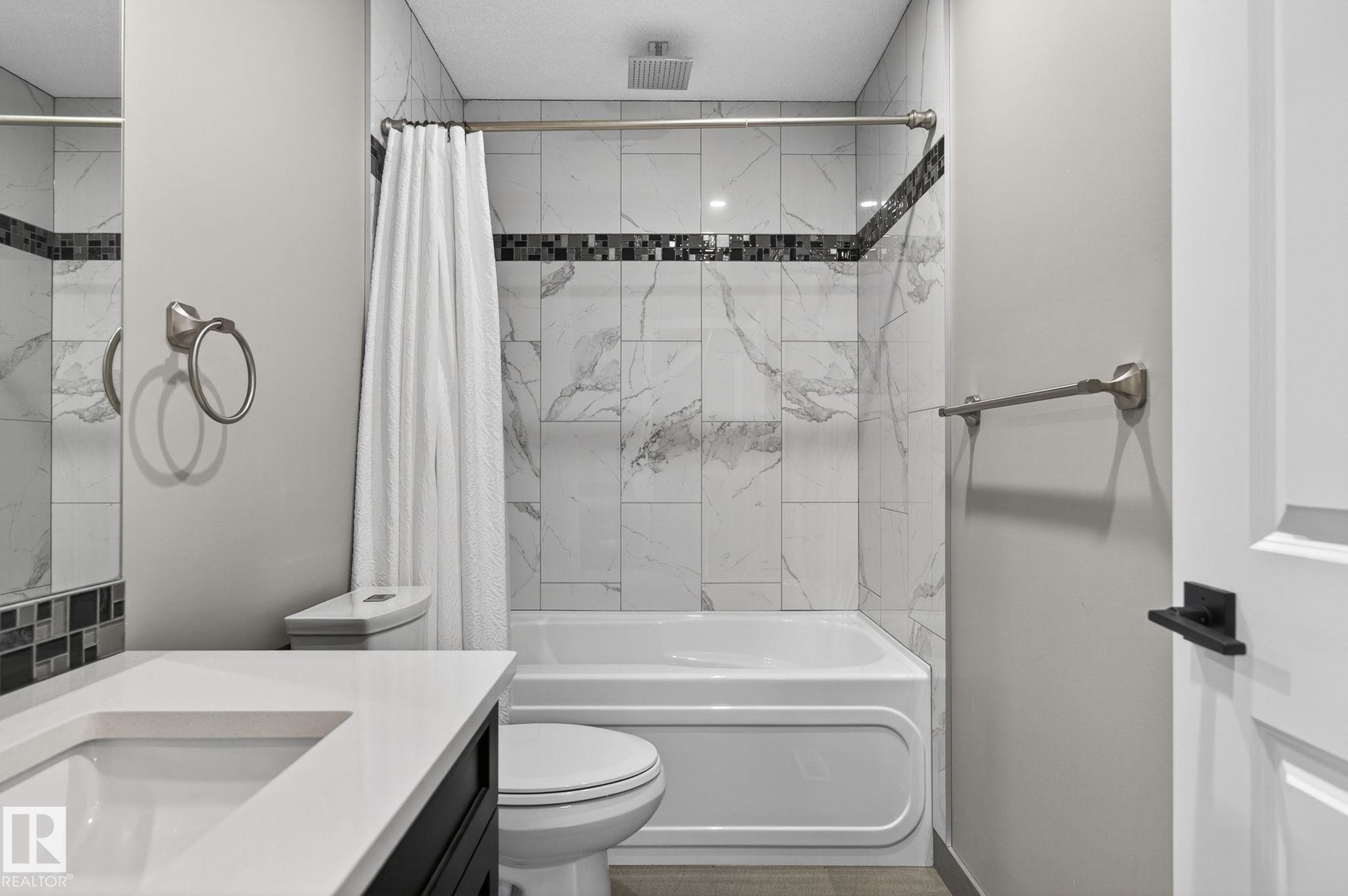 Bathroom featuring a built-in tub with shower, white and gray marbled wall tiles, decorative mosaic accent tile, white countertop with integrated sink, and dark wood-finish vanity - 8809 148 Street, Edmonton, AB - Indoor Photo Showing Bathroom