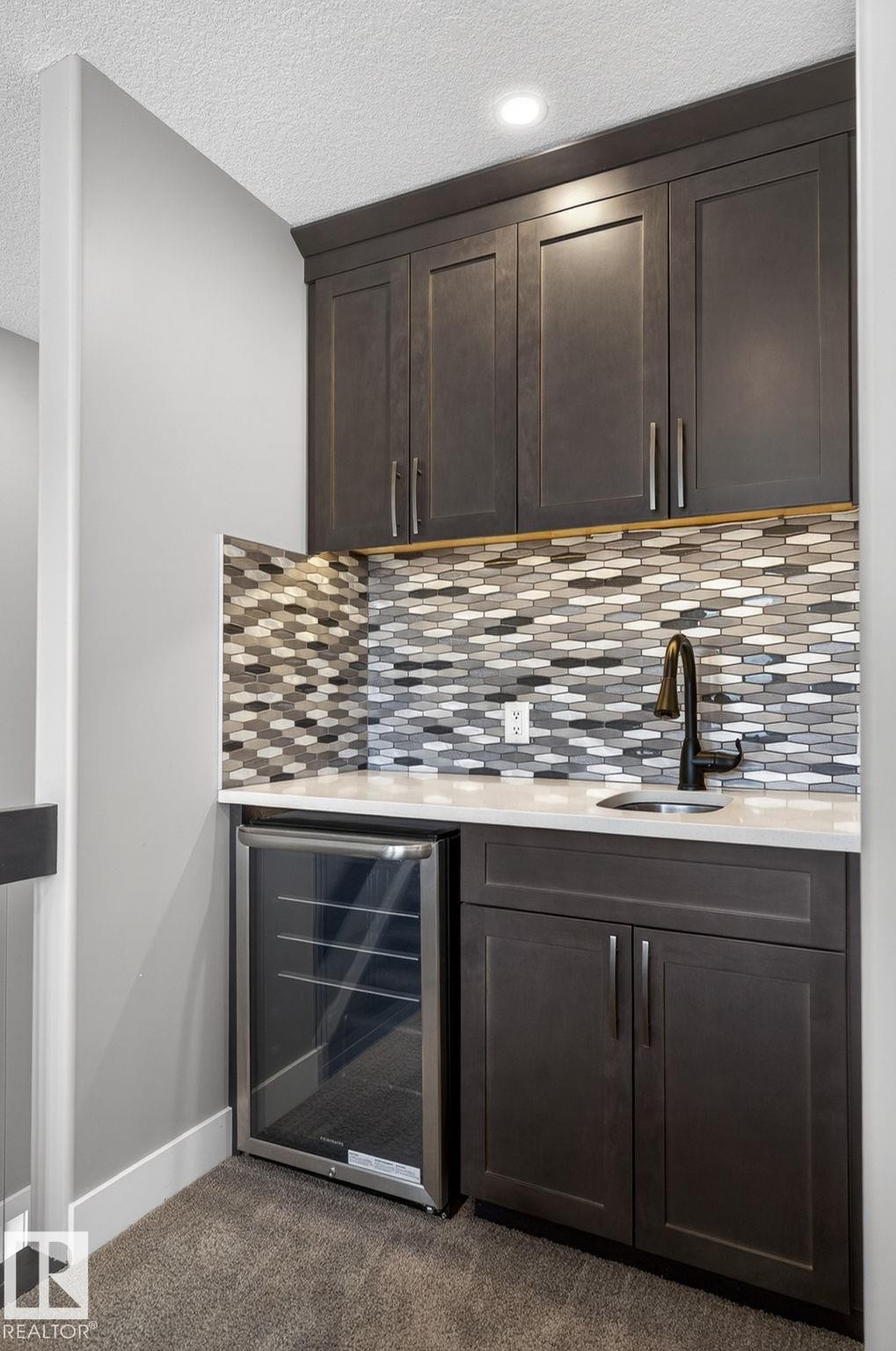 Wet bar with dark wood-finish cabinetry, a patterned tile backsplash, white countertop, and under-counter beverage refrigerator - 8809 148 Street, Edmonton, AB - Indoor