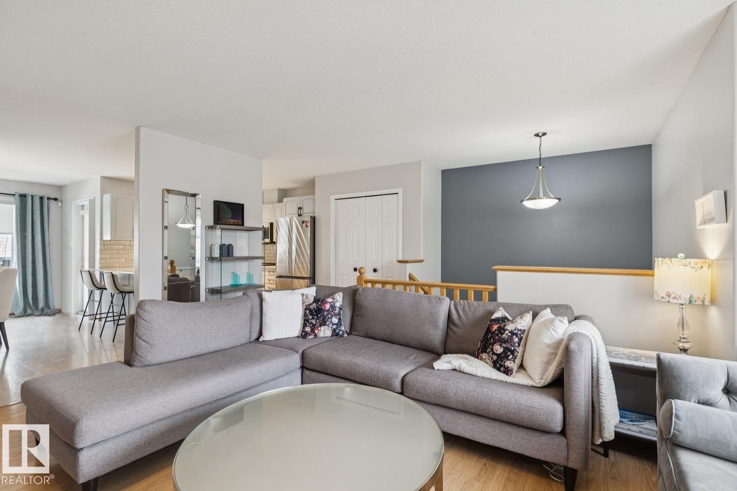 Hardwood-finish flooring throughout, featuring a kitchen with a stainless steel refrigerator and built-in cabinetry, and a dining area with a breakfast bar - 1 225 Blackburn Drive E, Edmonton, AB
