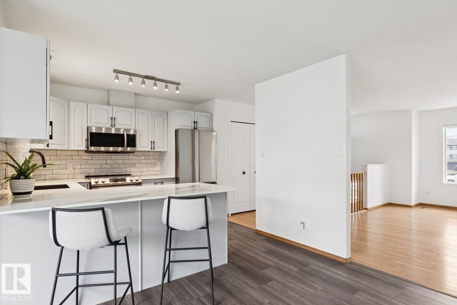 Modern kitchen featuring a large island with seating, white shaker-style cabinetry, stainless steel appliances, a white subway tile backsplash, and track lighting - 1 225 Blackburn Drive E, Edmonton, AB