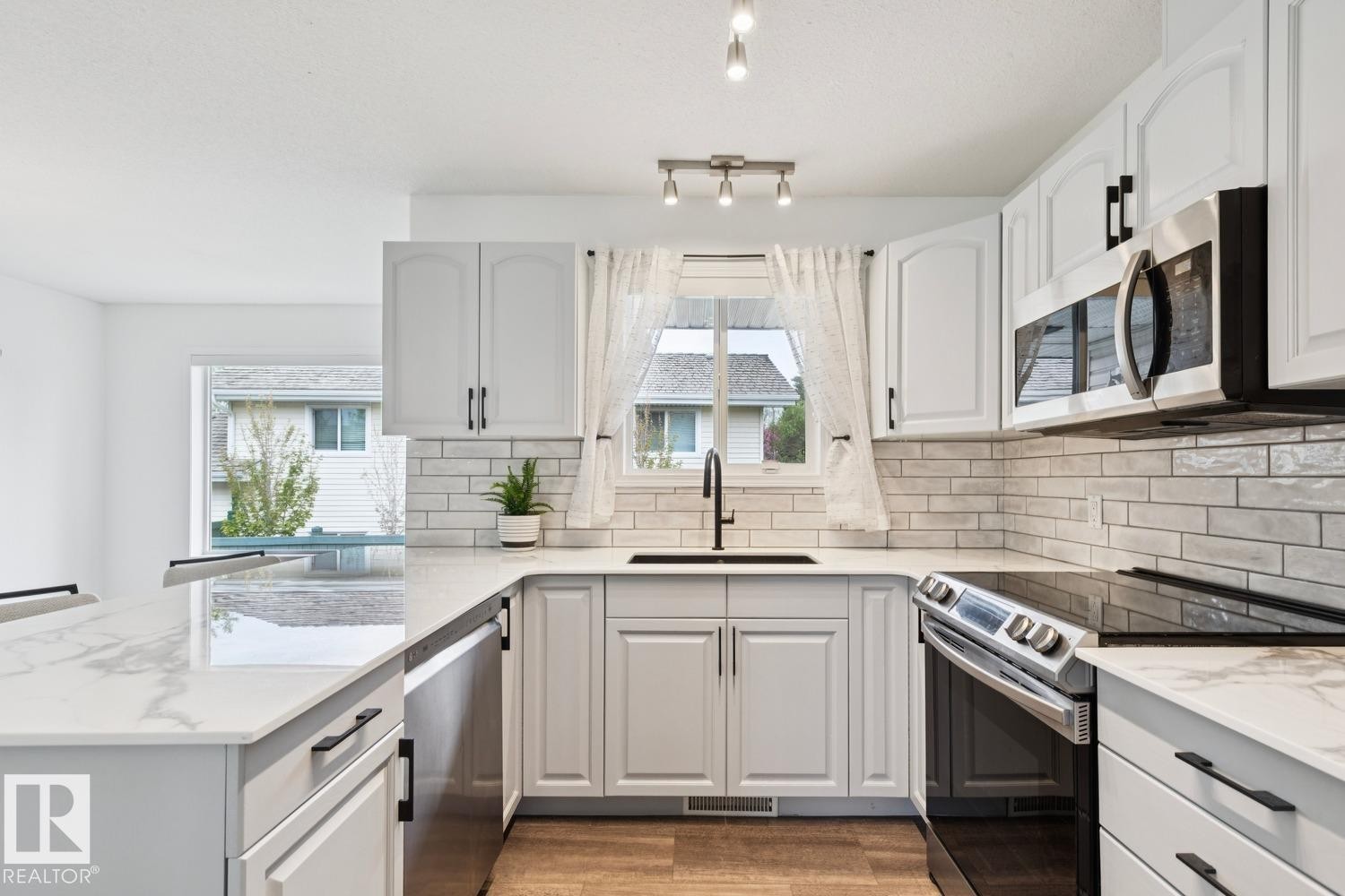 White cabinetry kitchen featuring a subway tile backsplash, light-toned countertops, stainless steel appliances, and wood-finish flooring - 1 225 Blackburn Drive E, Edmonton, AB