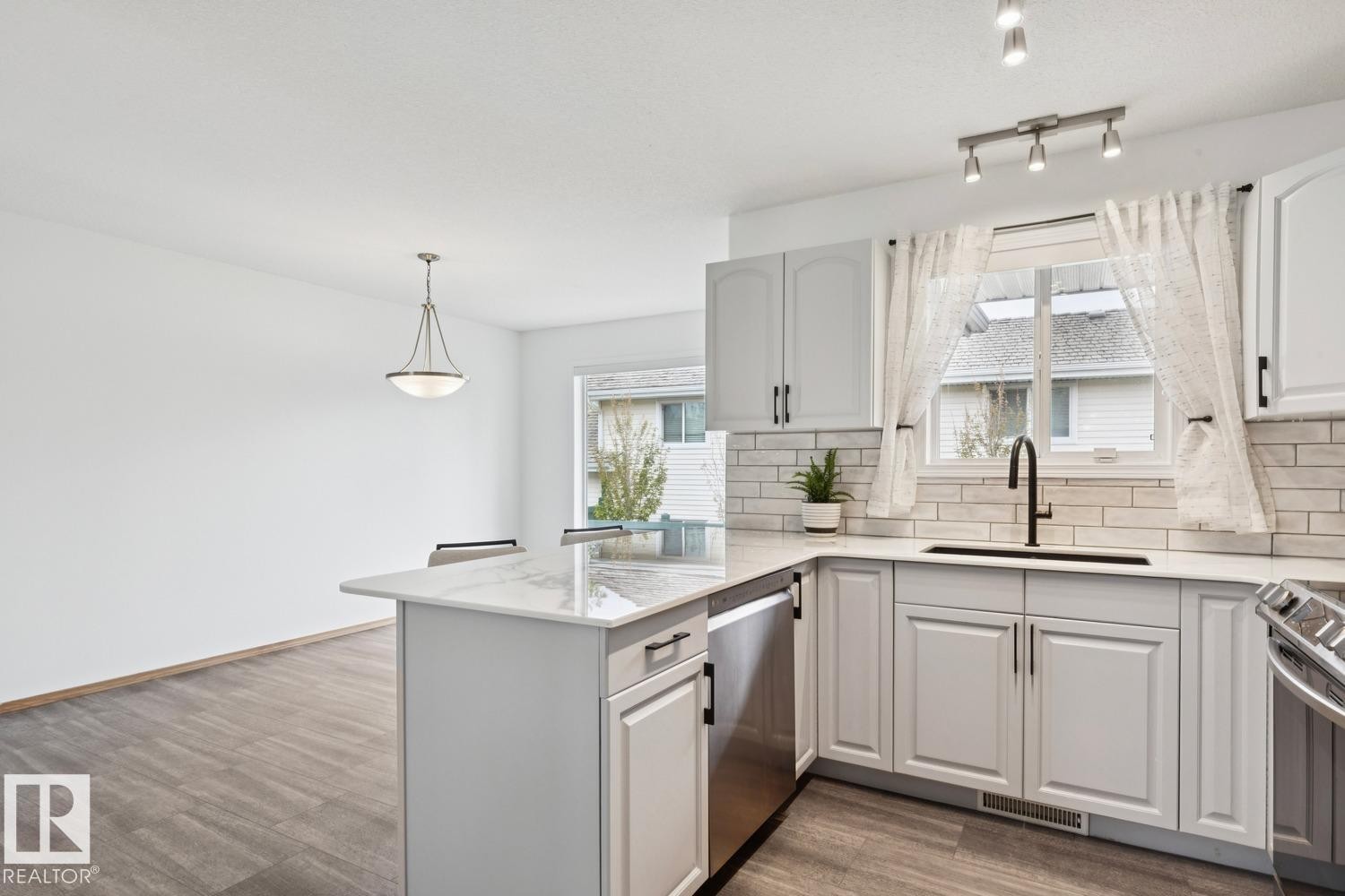 Modern kitchen featuring white cabinetry, light-toned countertops, a subway tile backsplash, and stainless steel appliances - 1 225 Blackburn Drive E, Edmonton, AB