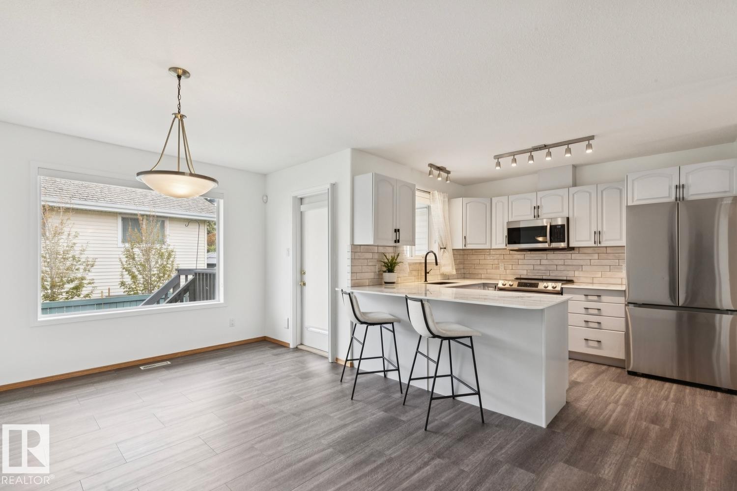 Bright kitchen and dining area featuring white cabinetry, stainless steel appliances, a subway tile backsplash, and a central island with a breakfast bar - 1 225 Blackburn Drive E, Edmonton, AB
