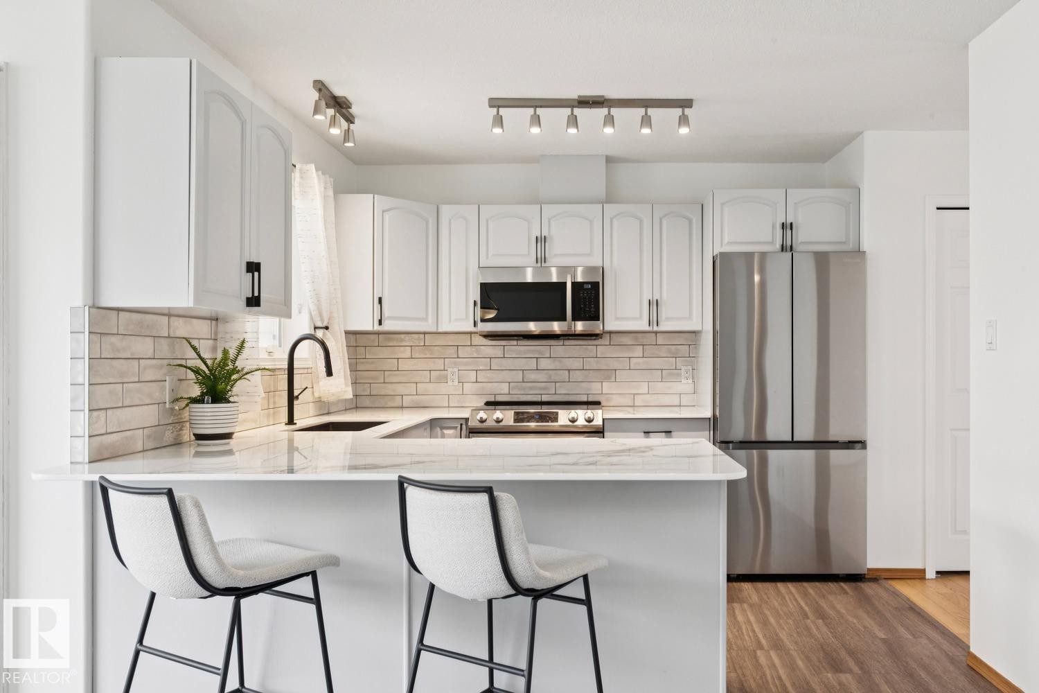 U-shaped kitchen featuring white cabinetry, stainless steel appliances, light-toned subway tile backsplash, white countertops, and wood-finish flooring - 1 225 Blackburn Drive E, Edmonton, AB