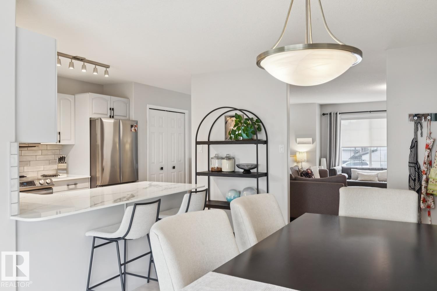 Bright kitchen featuring white cabinetry, stainless steel appliances, a subway tile backsplash, and a breakfast bar with stone-finish countertops - 1 225 Blackburn Drive E, Edmonton, AB