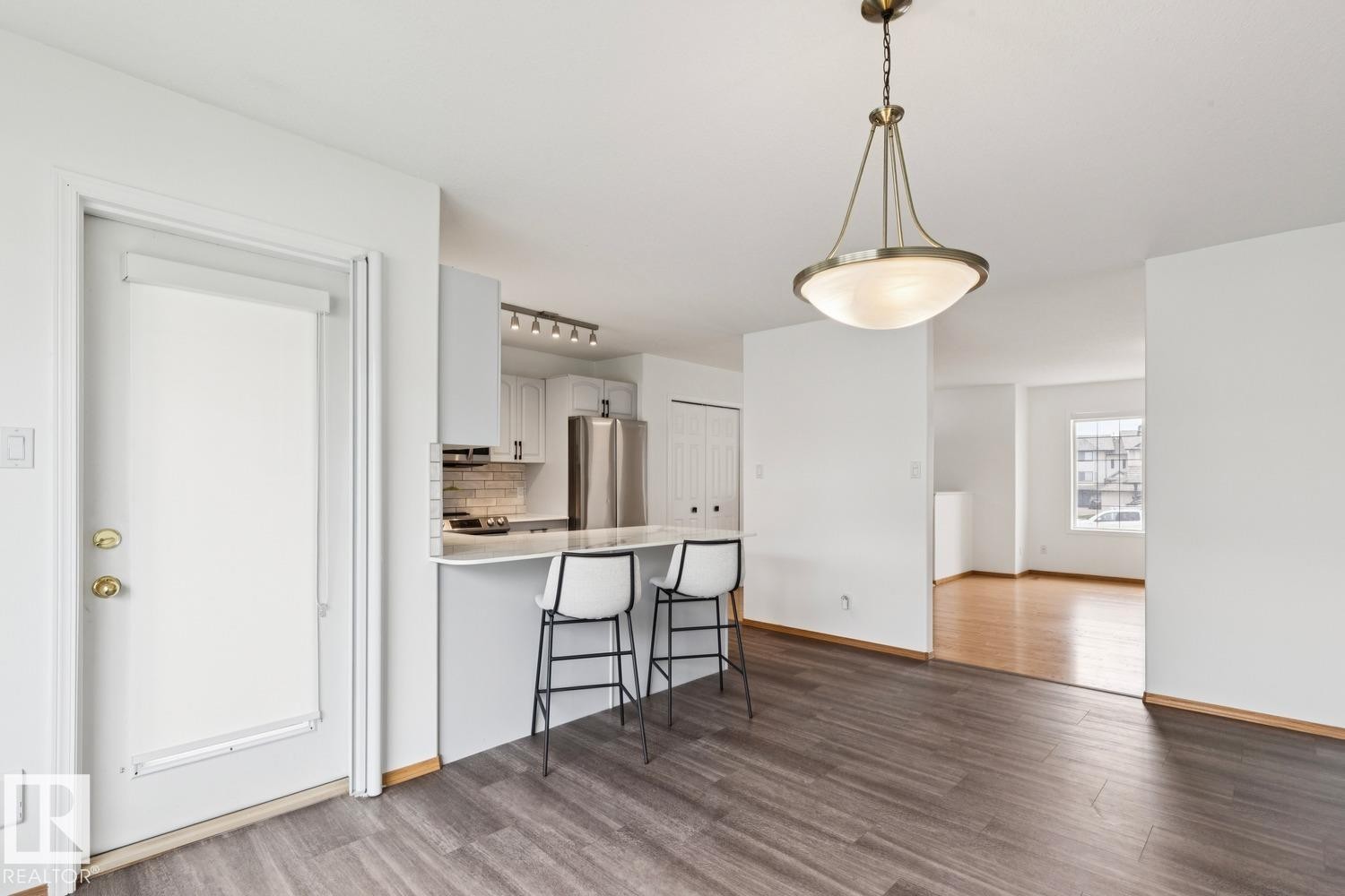 Open-concept living area featuring wood-finish flooring, a contemporary kitchen with stainless steel appliances, and a breakfast bar with seating - 1 225 Blackburn Drive E, Edmonton, AB