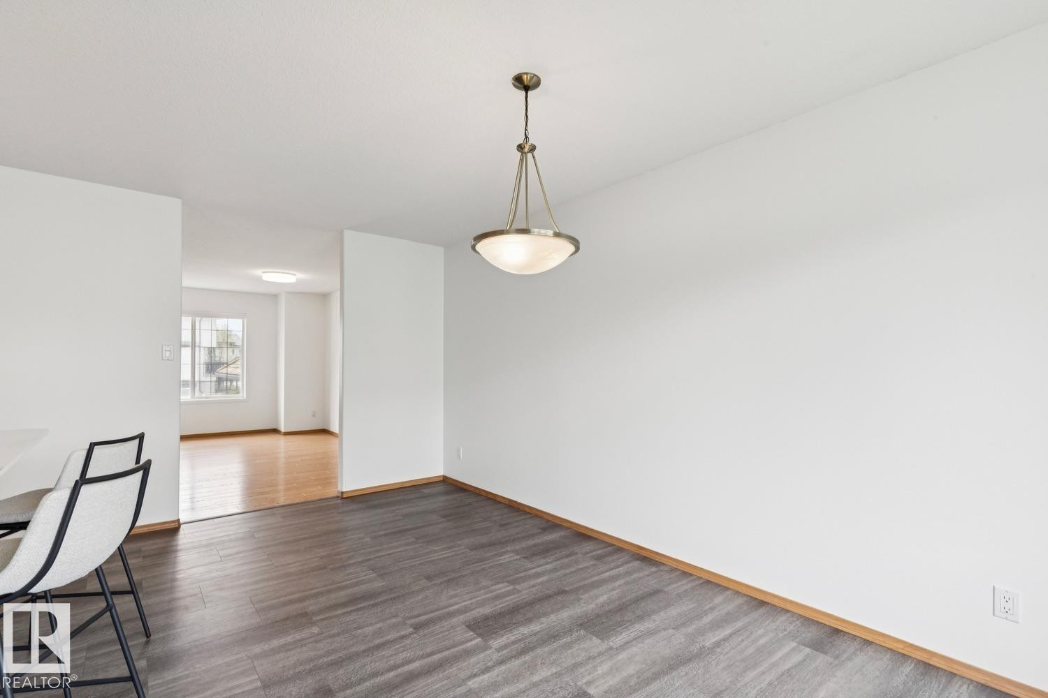 Spacious room with wood-finish flooring, a contemporary pendant light fixture, and white walls - 1 225 Blackburn Drive E, Edmonton, AB