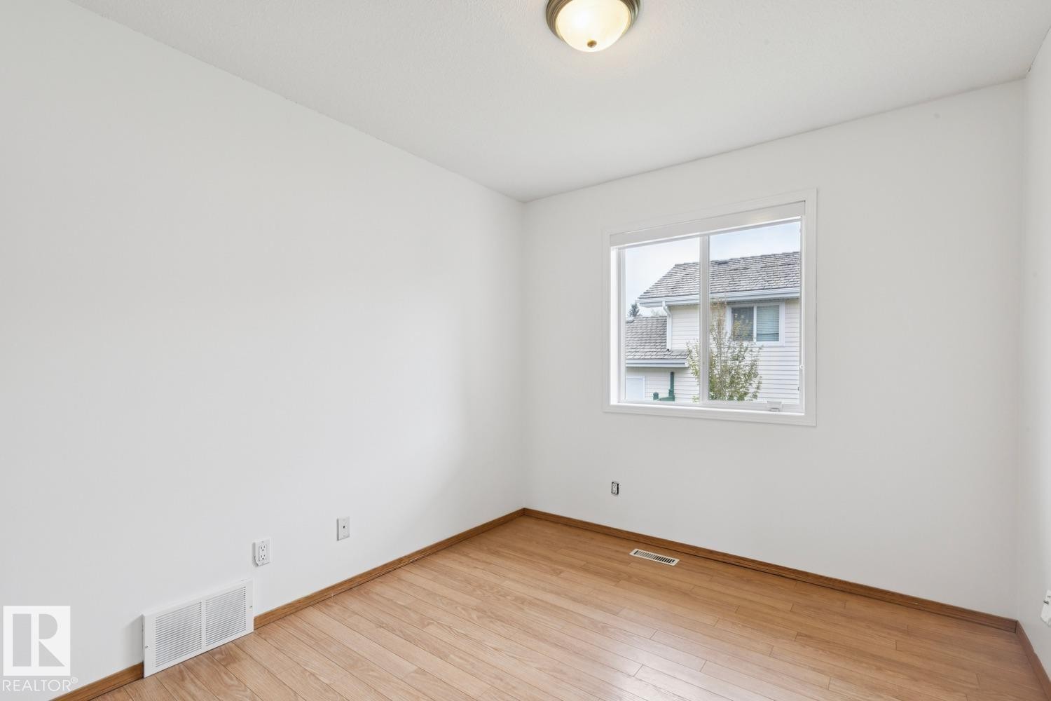 Room featuring wood-finish flooring, white baseboards, and a white window frame - 1 225 Blackburn Drive E, Edmonton, AB