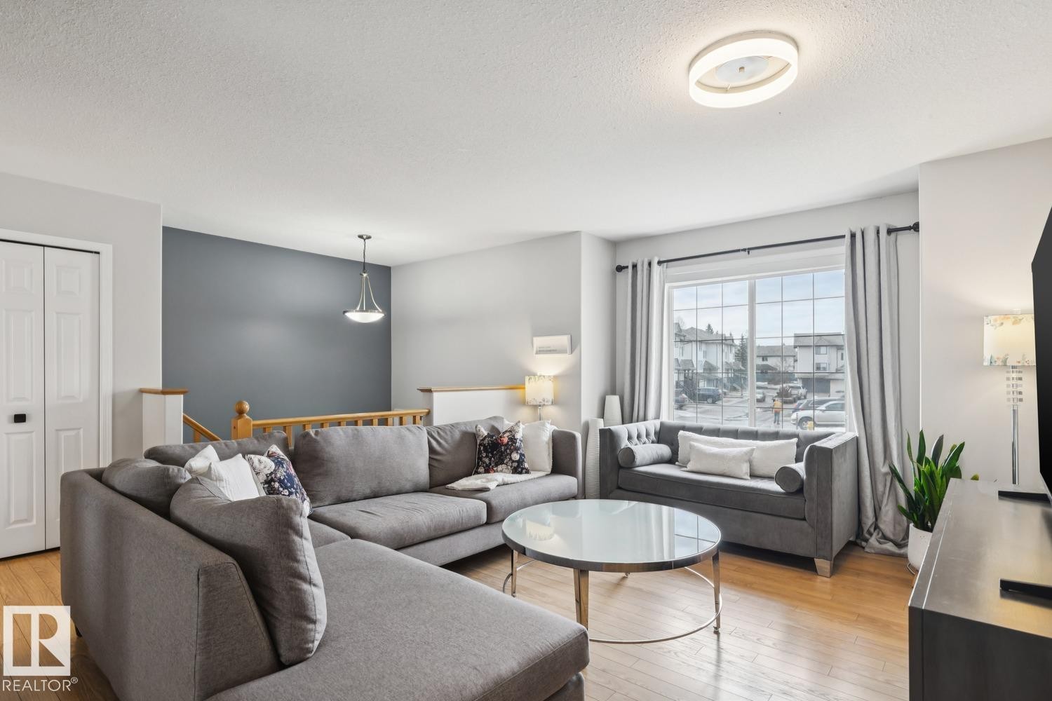 Open-concept living area featuring wood-finish flooring, a prominent window with vertical blinds, and a contemporary ceiling light fixture - 1 225 Blackburn Drive E, Edmonton, AB