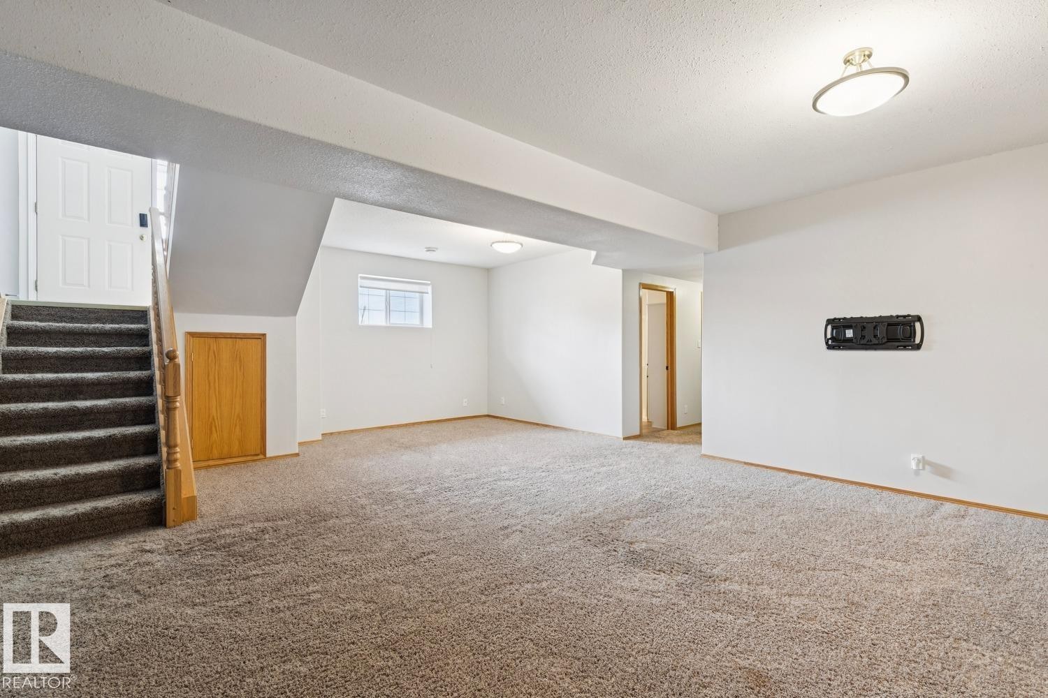 Open concept room with neutral carpeting, white walls, and a window for natural light - 1 225 Blackburn Drive E, Edmonton, AB