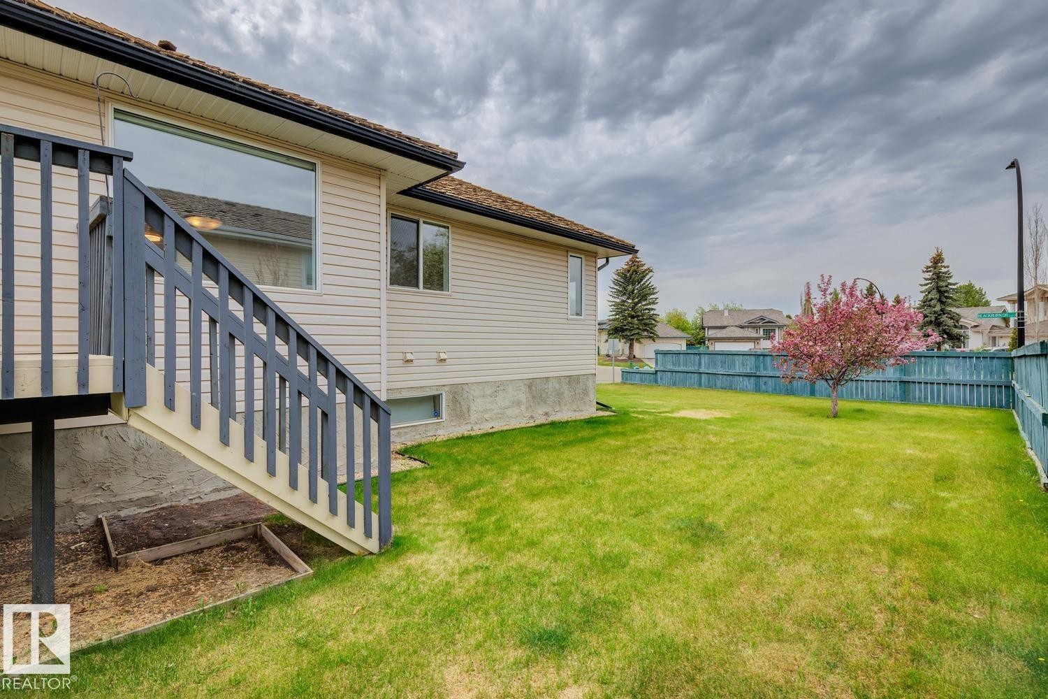 Expansive rear yard featuring a manicured lawn, painted wooden fencing, and a blooming tree - 1 225 Blackburn Drive E, Edmonton, AB