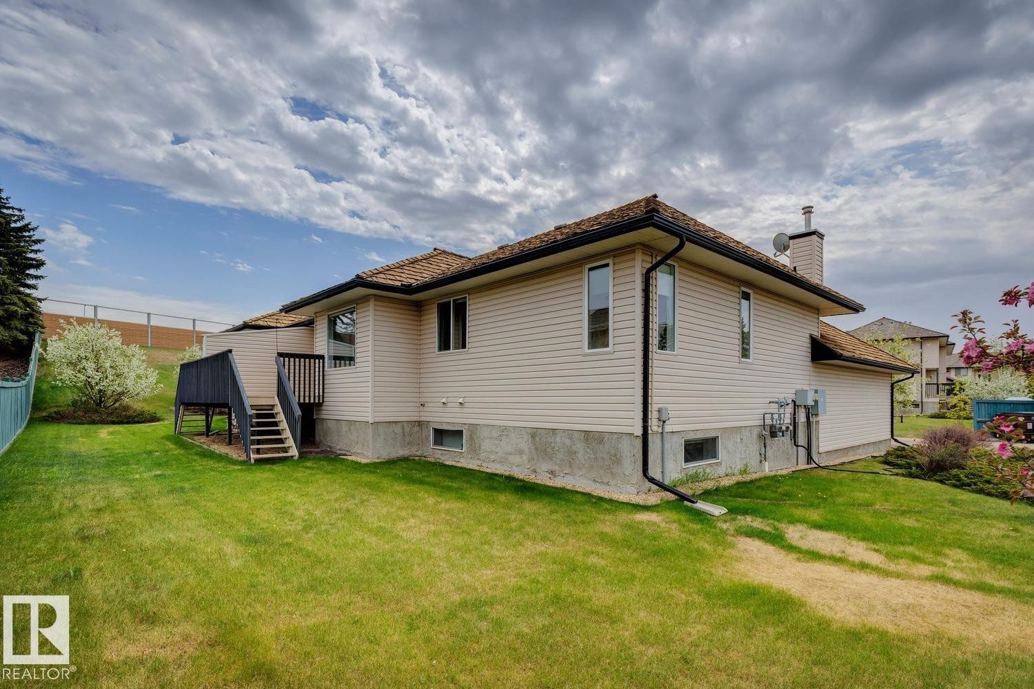 Expansive backyard featuring a manicured lawn, a two-level deck with dark wood-finish railings, and mature landscaping - 1 225 Blackburn Drive E, Edmonton, AB