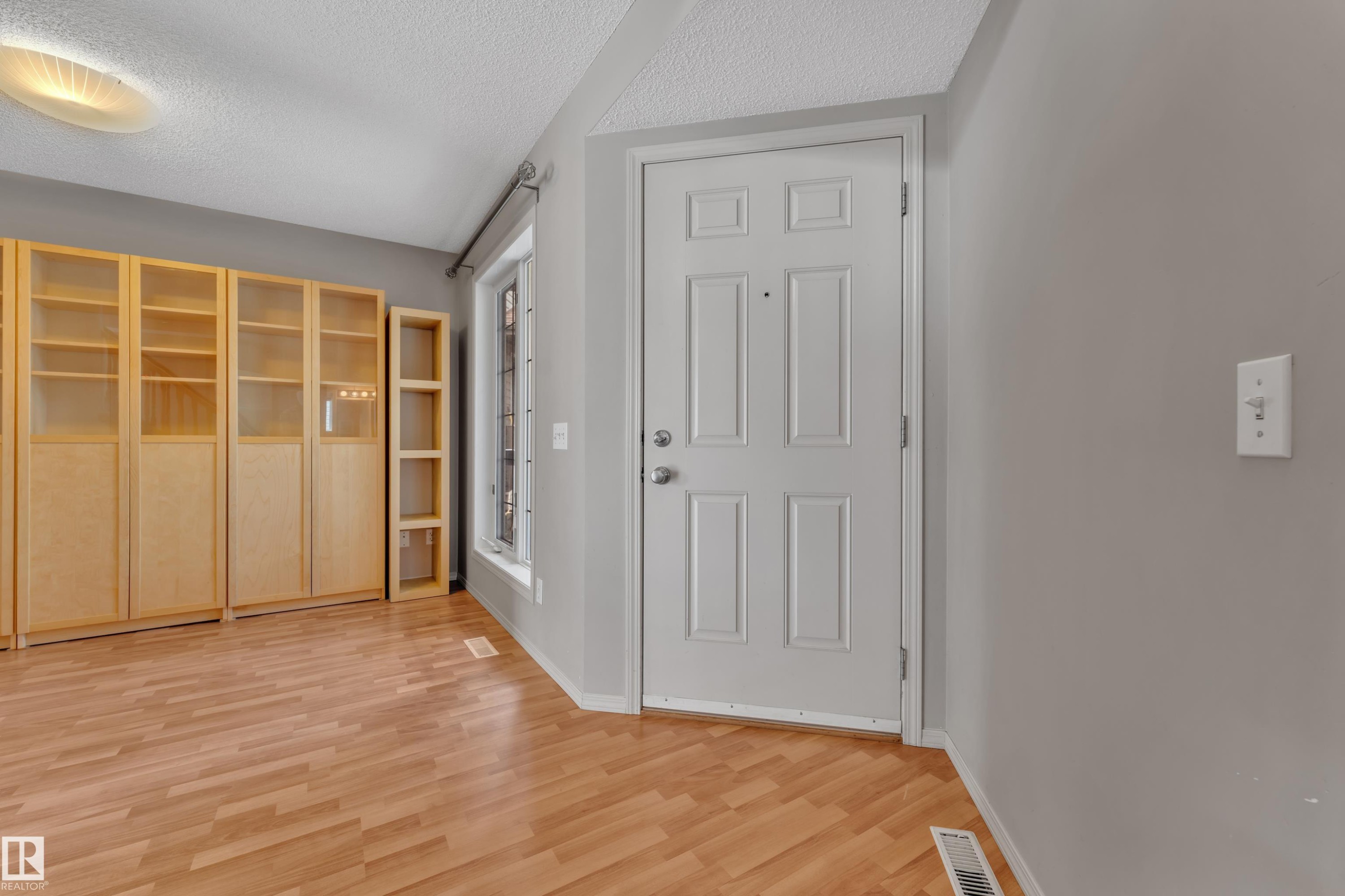 Entryway featuring wood-finish flooring, a white paneled door, and built-in wood-toned shelving with glass-front cabinets - 14031 136 Street, Edmonton, AB