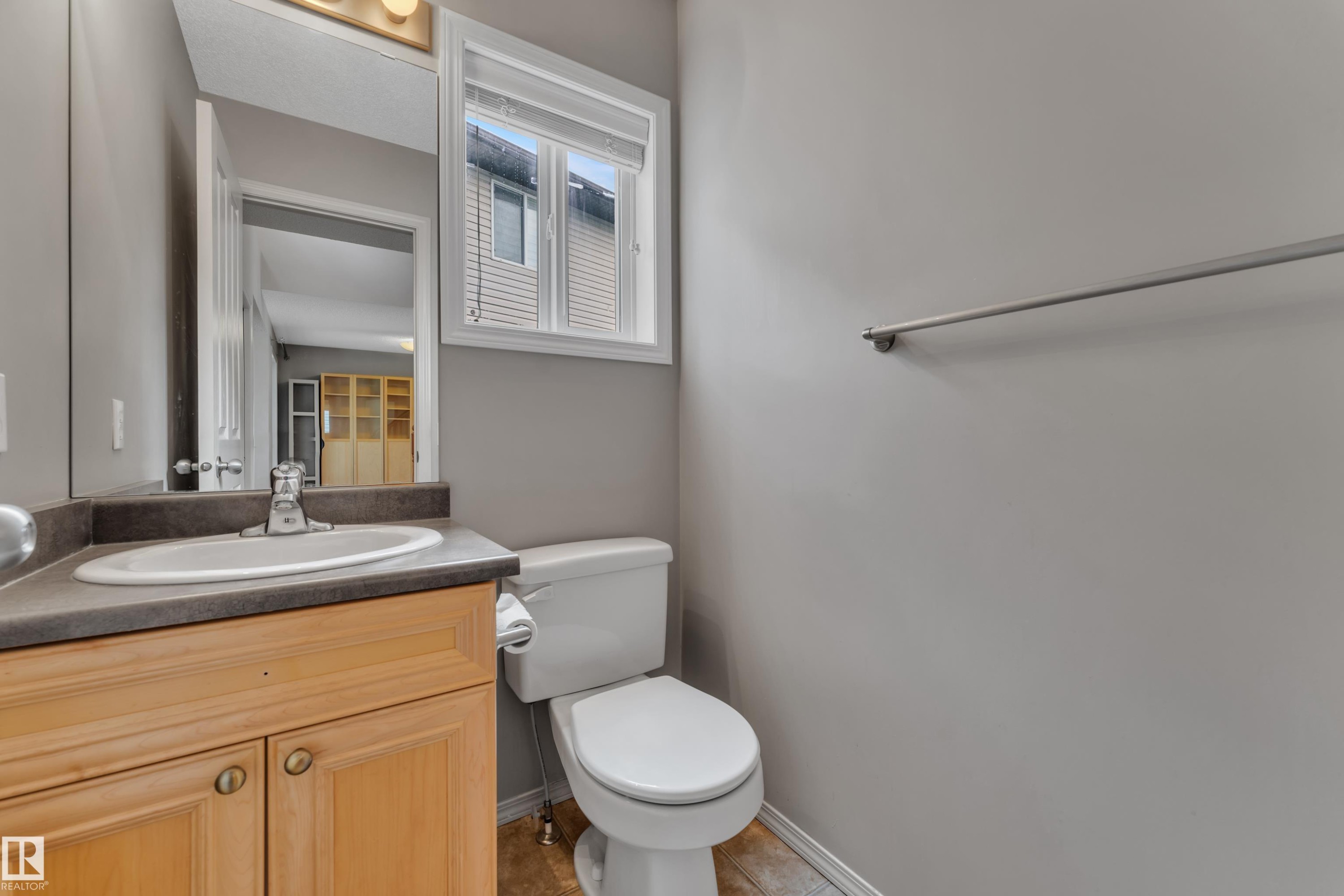 Bathroom featuring a wood-finish vanity with an integrated sink, a large wall mirror, and a window for natural light - 14031 136 Street, Edmonton, AB