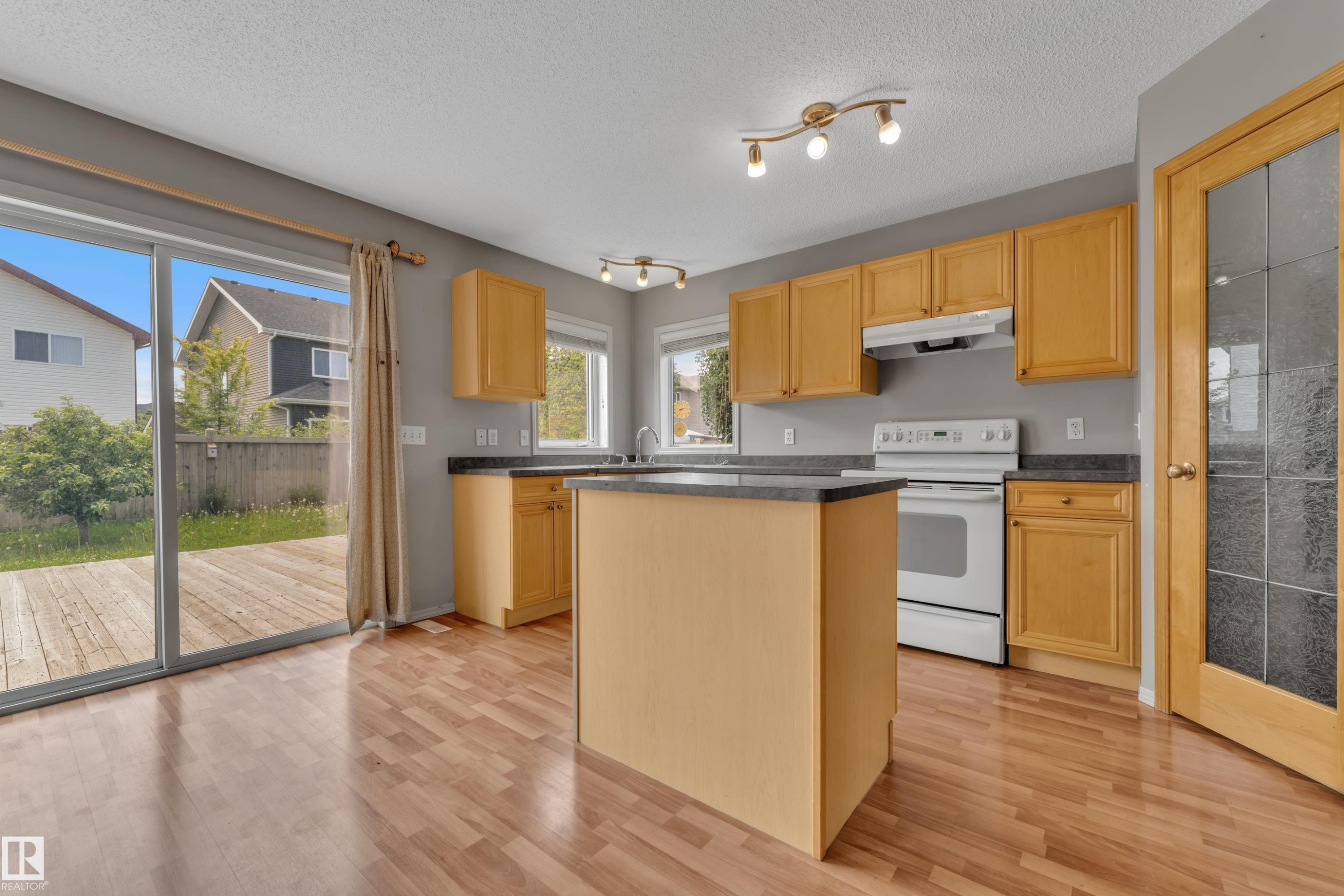Kitchen featuring wood-finish flooring, light wood cabinetry, a central island, a built-in range, and dark countertops - 14031 136 Street, Edmonton, AB