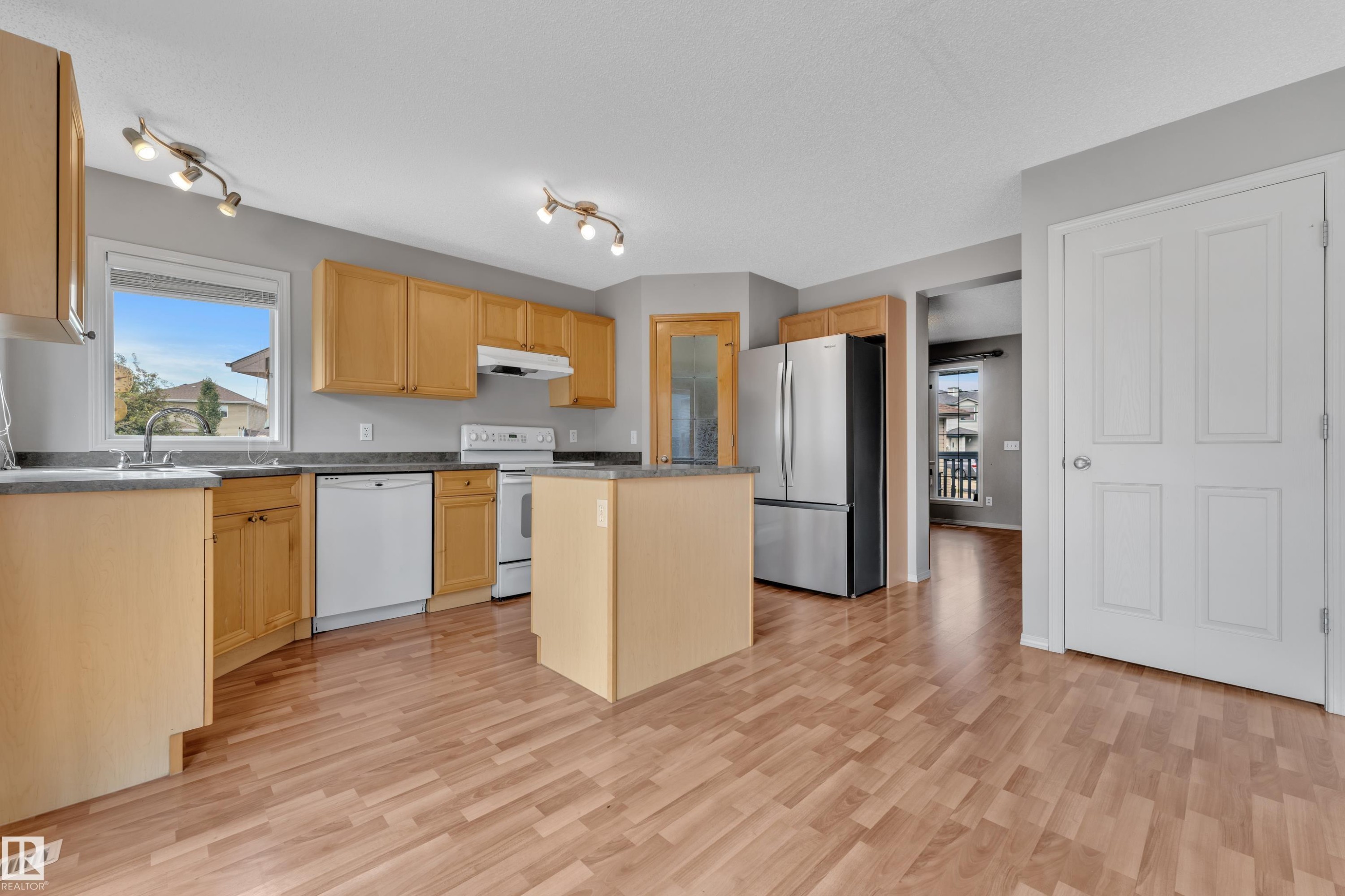 Kitchen featuring light wood-finish cabinetry, a central island, stainless steel appliances, a double-basin sink, and overhead track lighting - 14031 136 Street, Edmonton, AB
