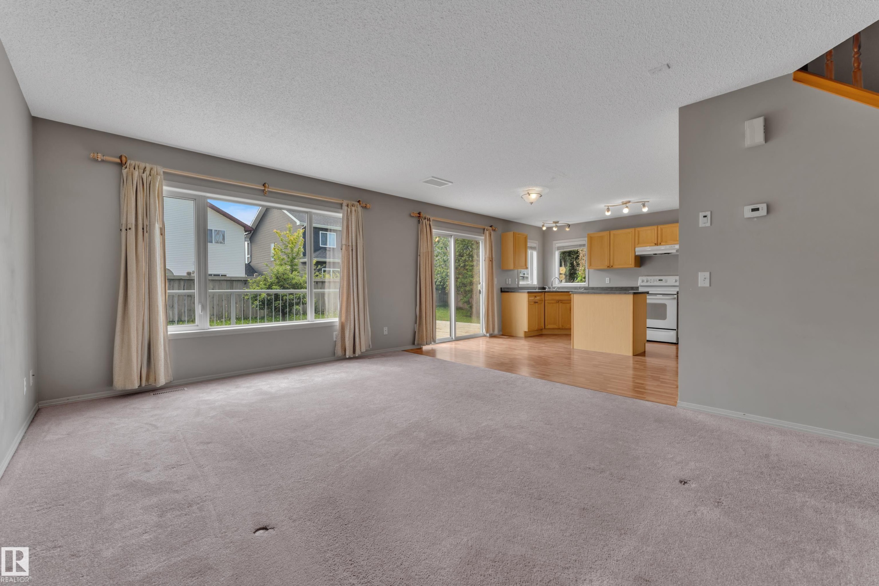 Expansive carpeted living area featuring a large picture window and sliding glass door - 14031 136 Street, Edmonton, AB