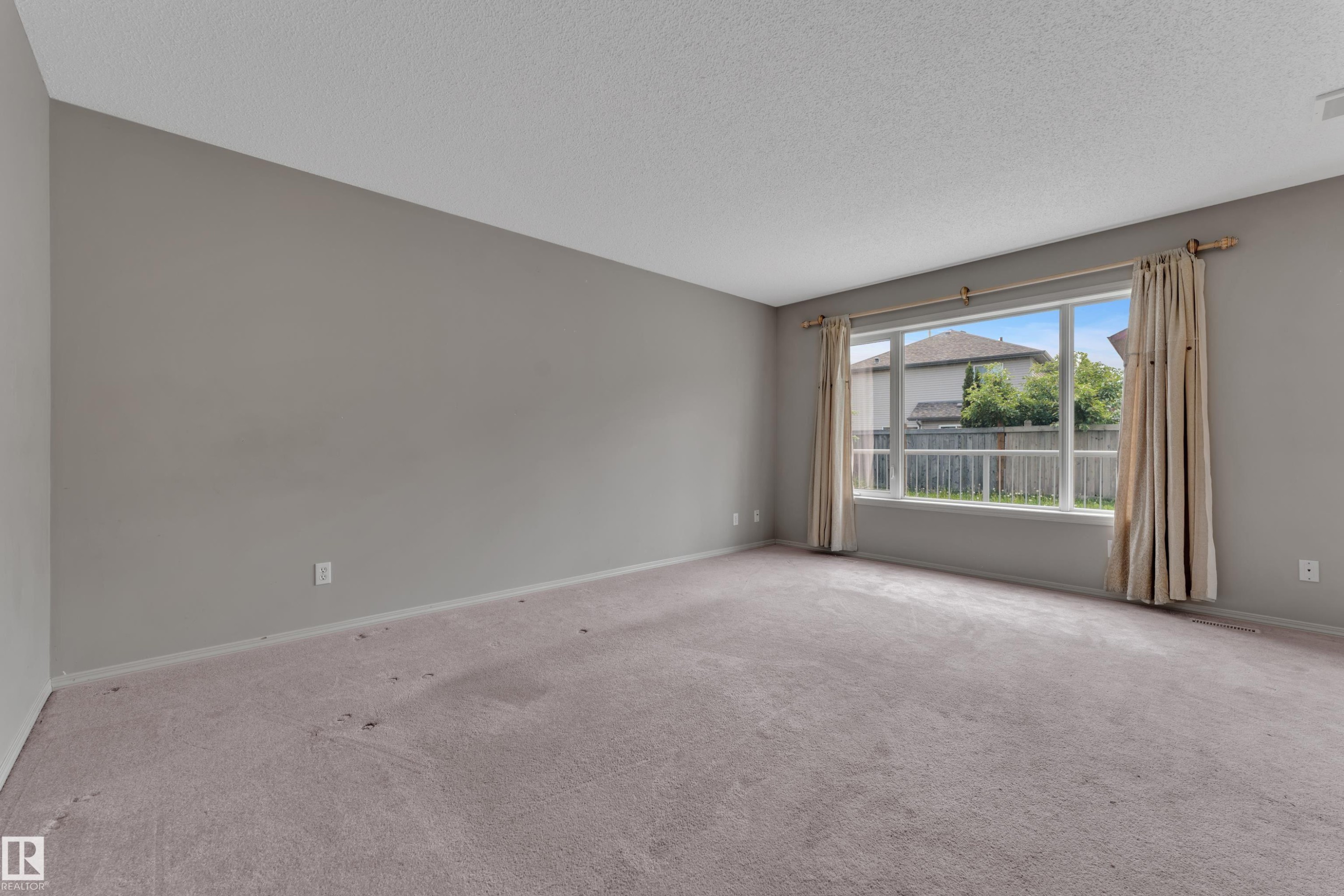 Spacious interior room featuring a large multi-pane window with drapery rods, light-colored carpeting, and neutral wall paint - 14031 136 Street, Edmonton, AB