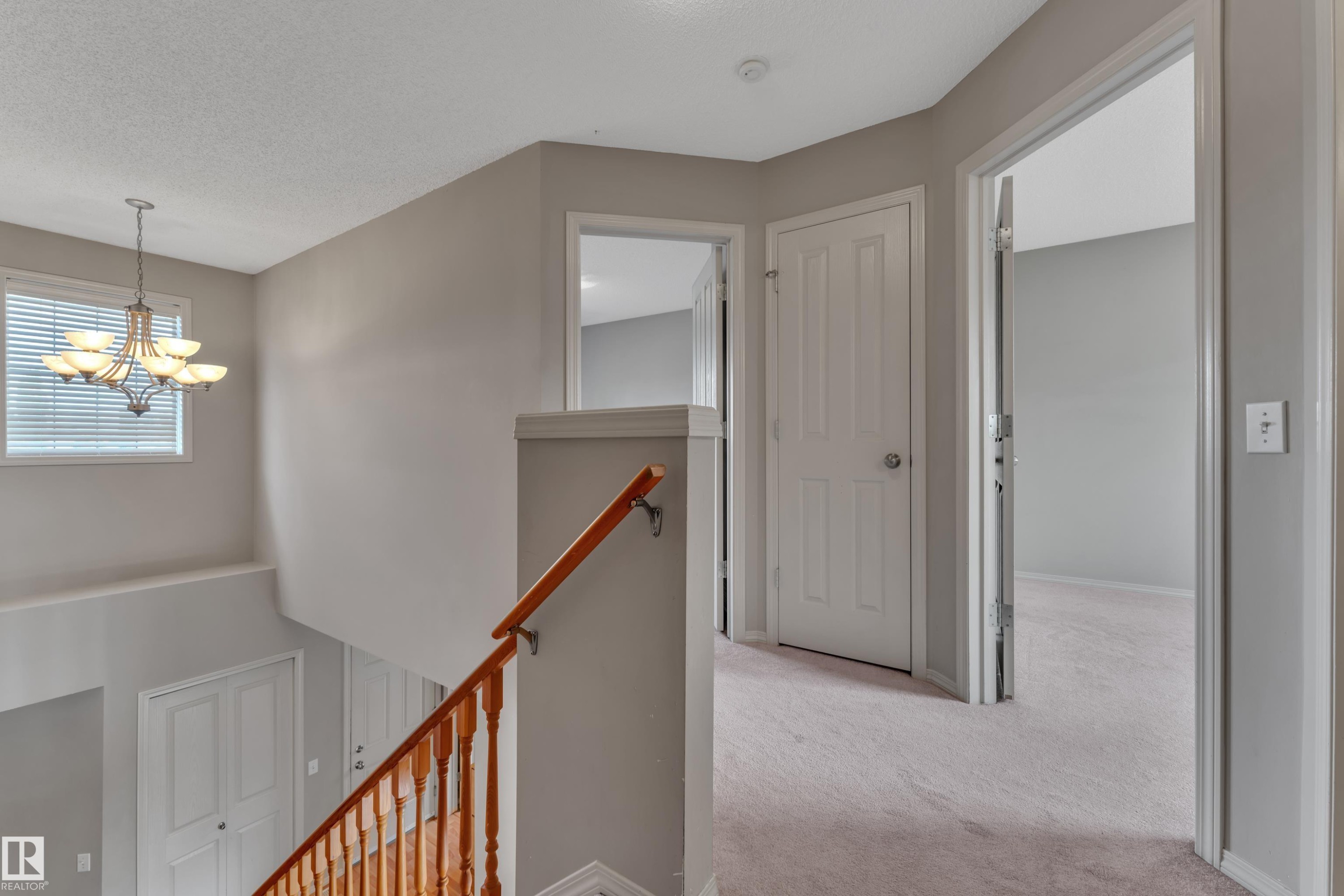 Second-story hallway featuring neutral paint, light-toned carpeting, and a traditional wood banister - 14031 136 Street, Edmonton, AB