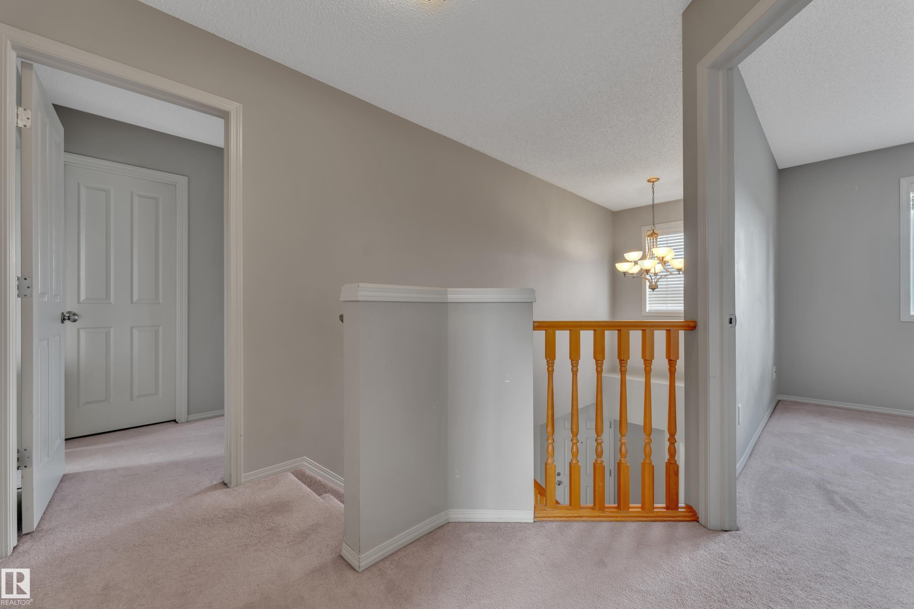 Upper-level landing featuring neutral carpeting, a staircase with wood newel posts and balusters, and a contemporary chandelier - 14031 136 Street, Edmonton, AB