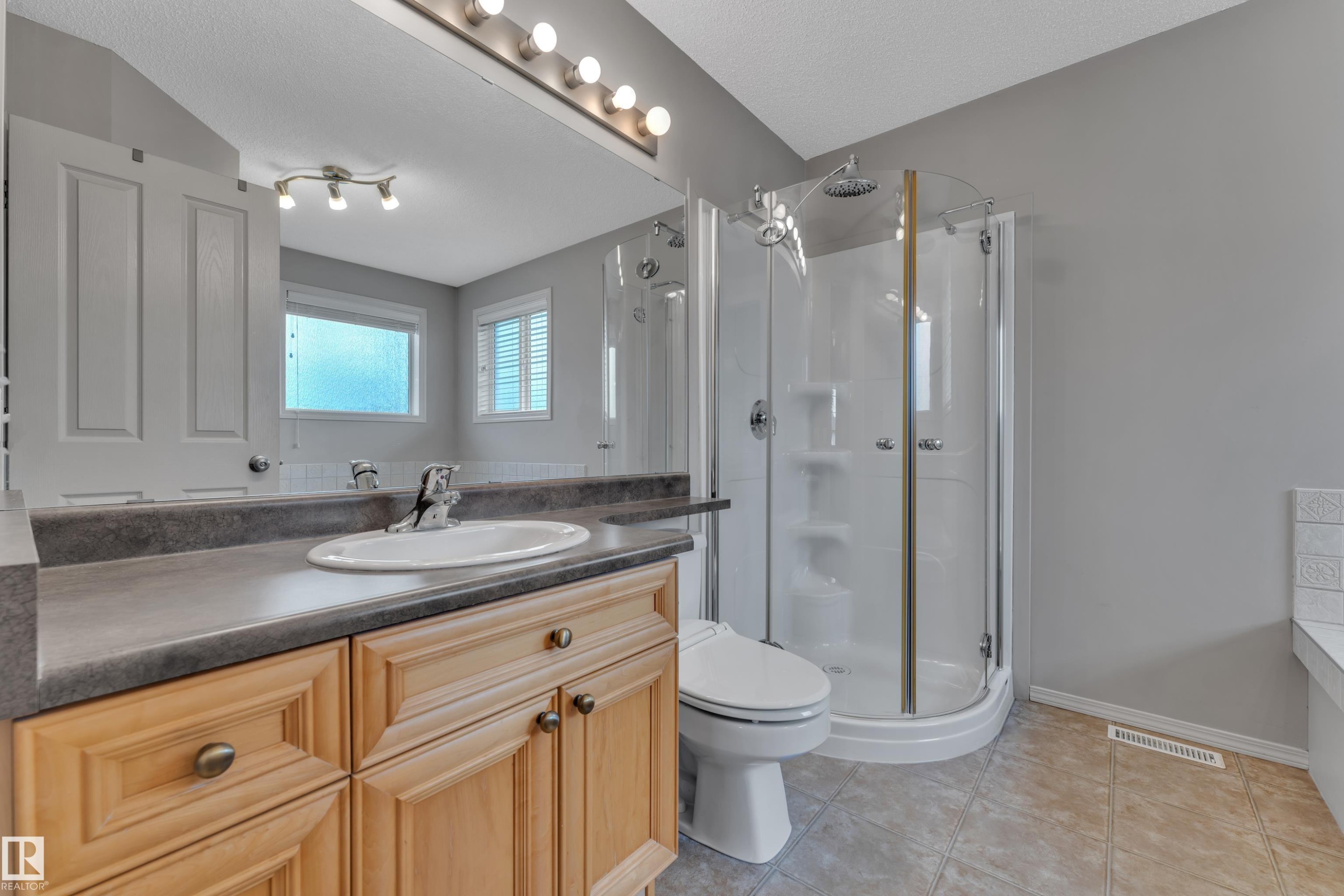 Bathroom featuring a light wood-finish vanity with a single basin, grey countertop, and an adjacent glass-enclosed shower - 14031 136 Street, Edmonton, AB