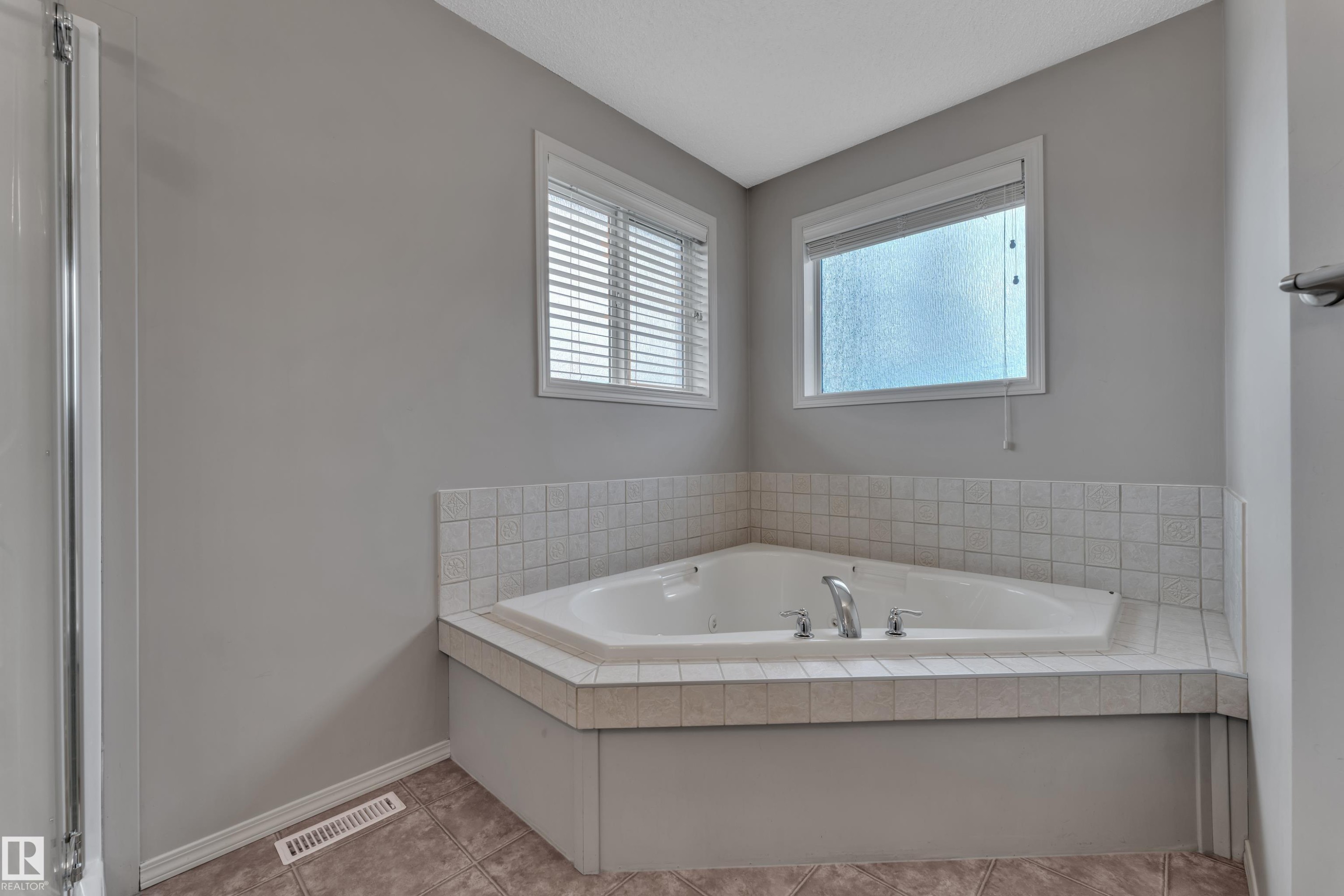 Corner jacuzzi tub with tiled surround, two windows with blinds, and tile flooring - 14031 136 Street, Edmonton, AB