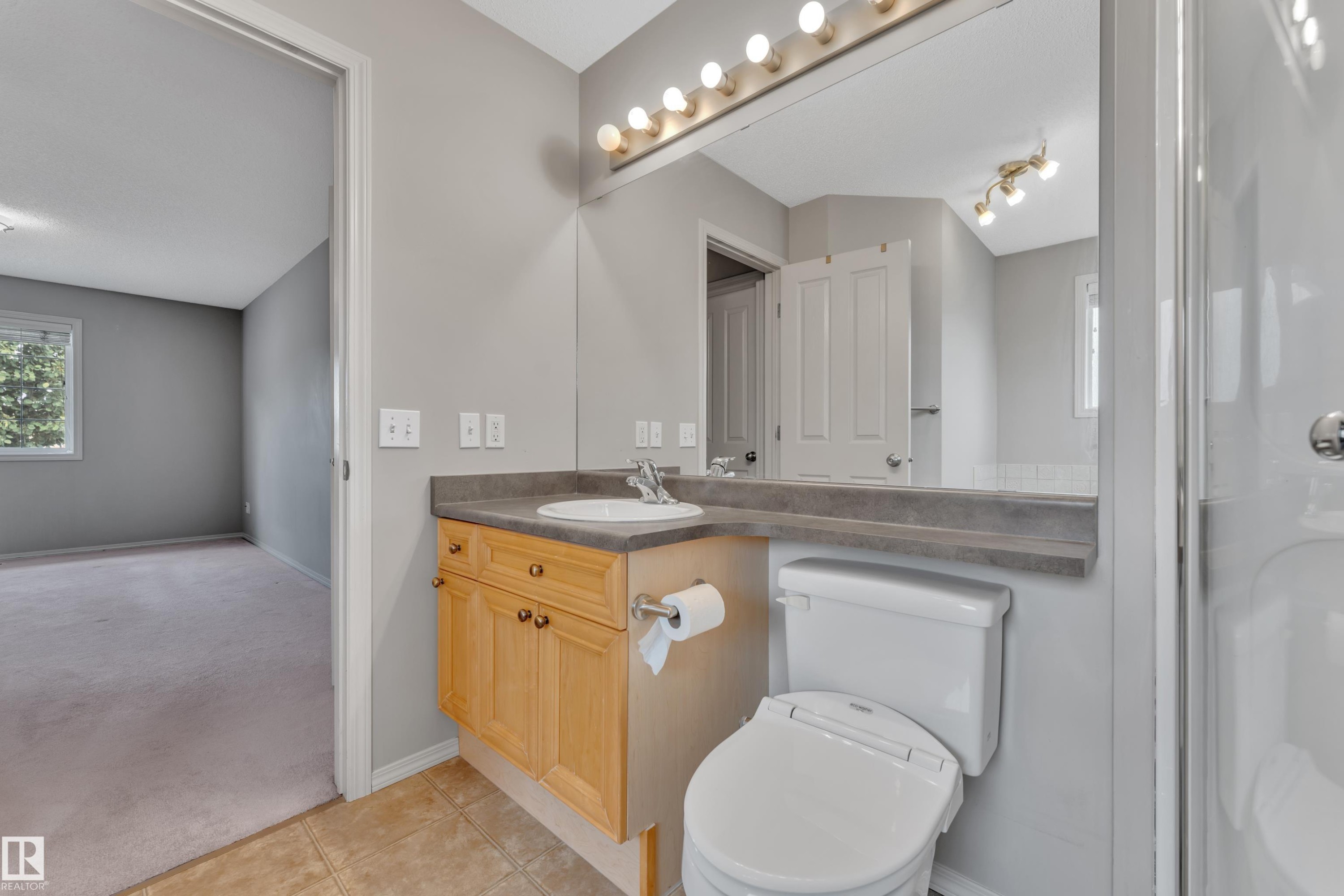 Bathroom vanity with a light wood-finish cabinet, integrated sink, and dark countertop - 14031 136 Street, Edmonton, AB