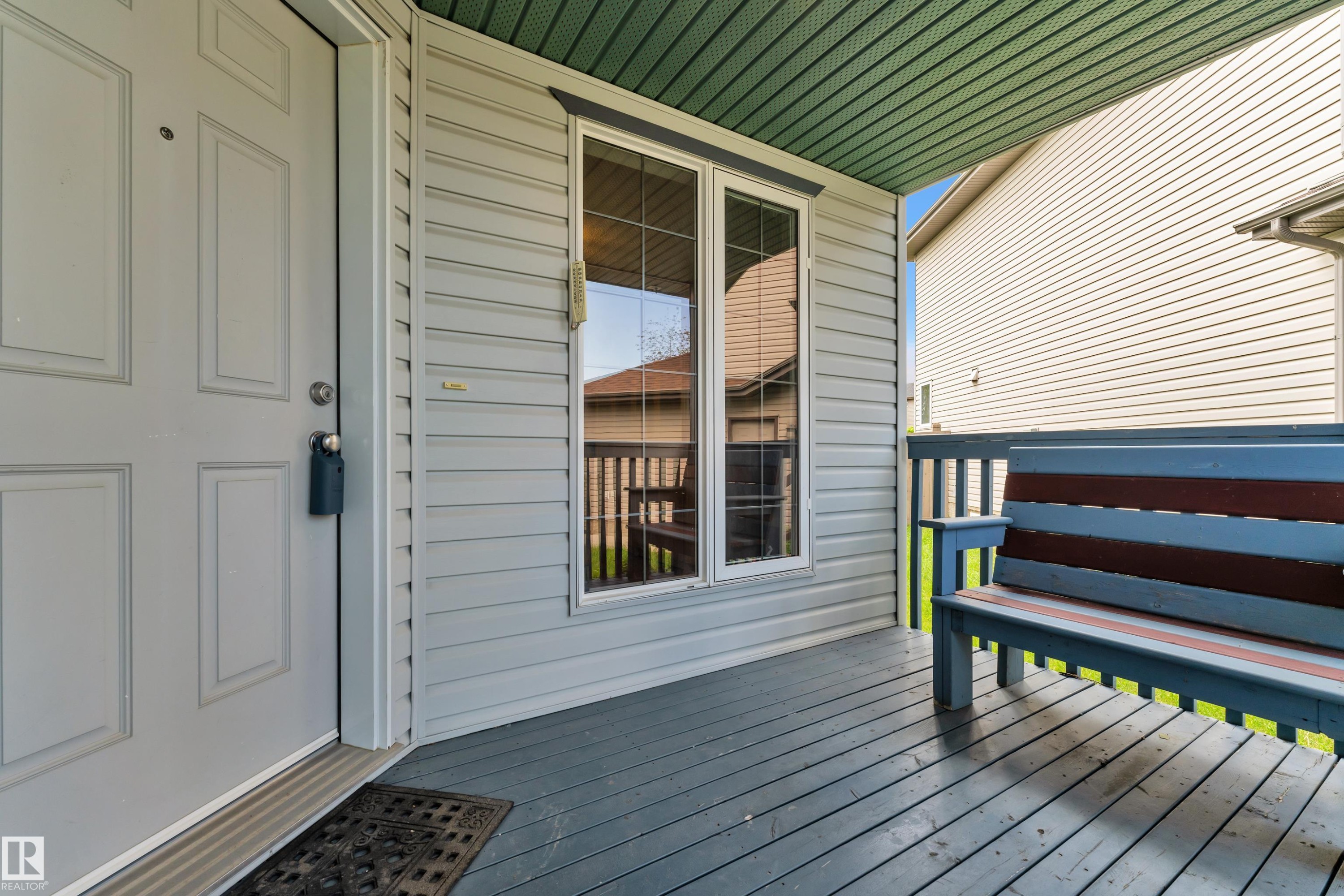 Covered front porch featuring a paneled door, vertical siding, and a beadboard ceiling - 14031 136 Street, Edmonton, AB