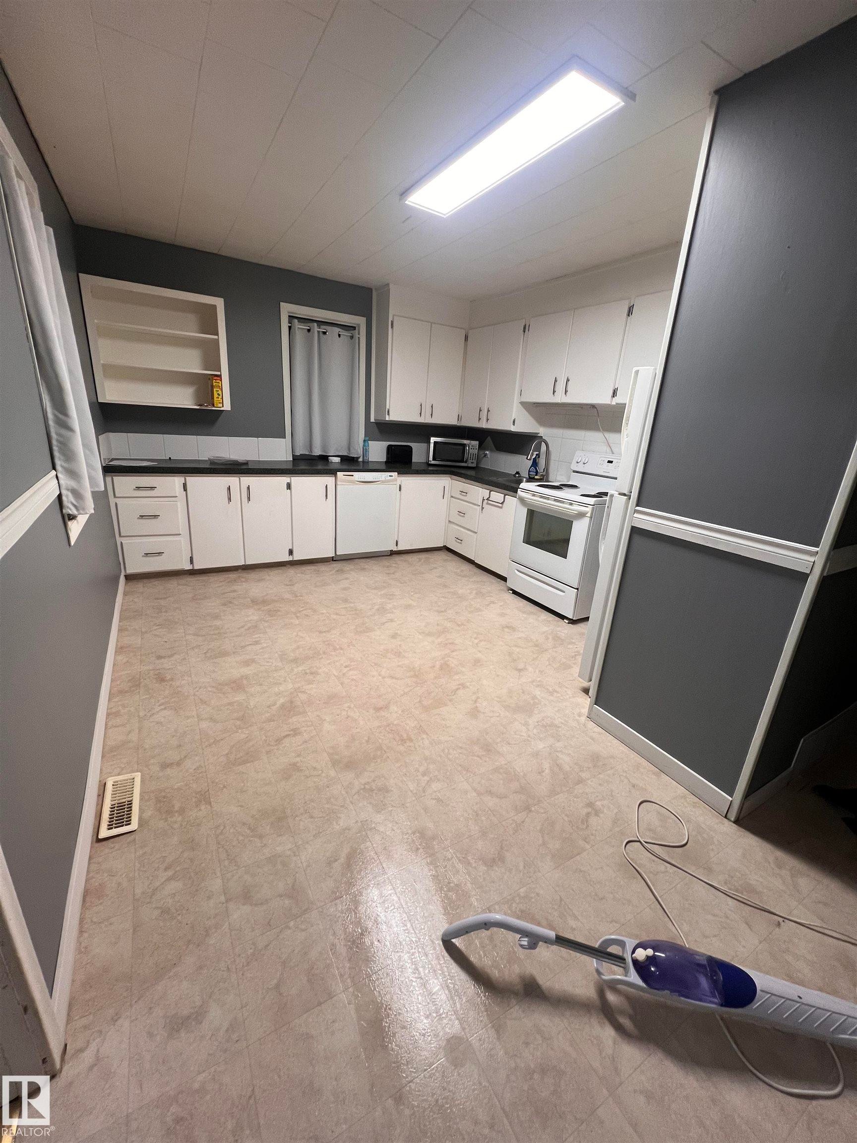 Spacious kitchen featuring extensive white cabinetry, dark countertops, and a white appliance suite - 69 Railway Avenue, Star, AB