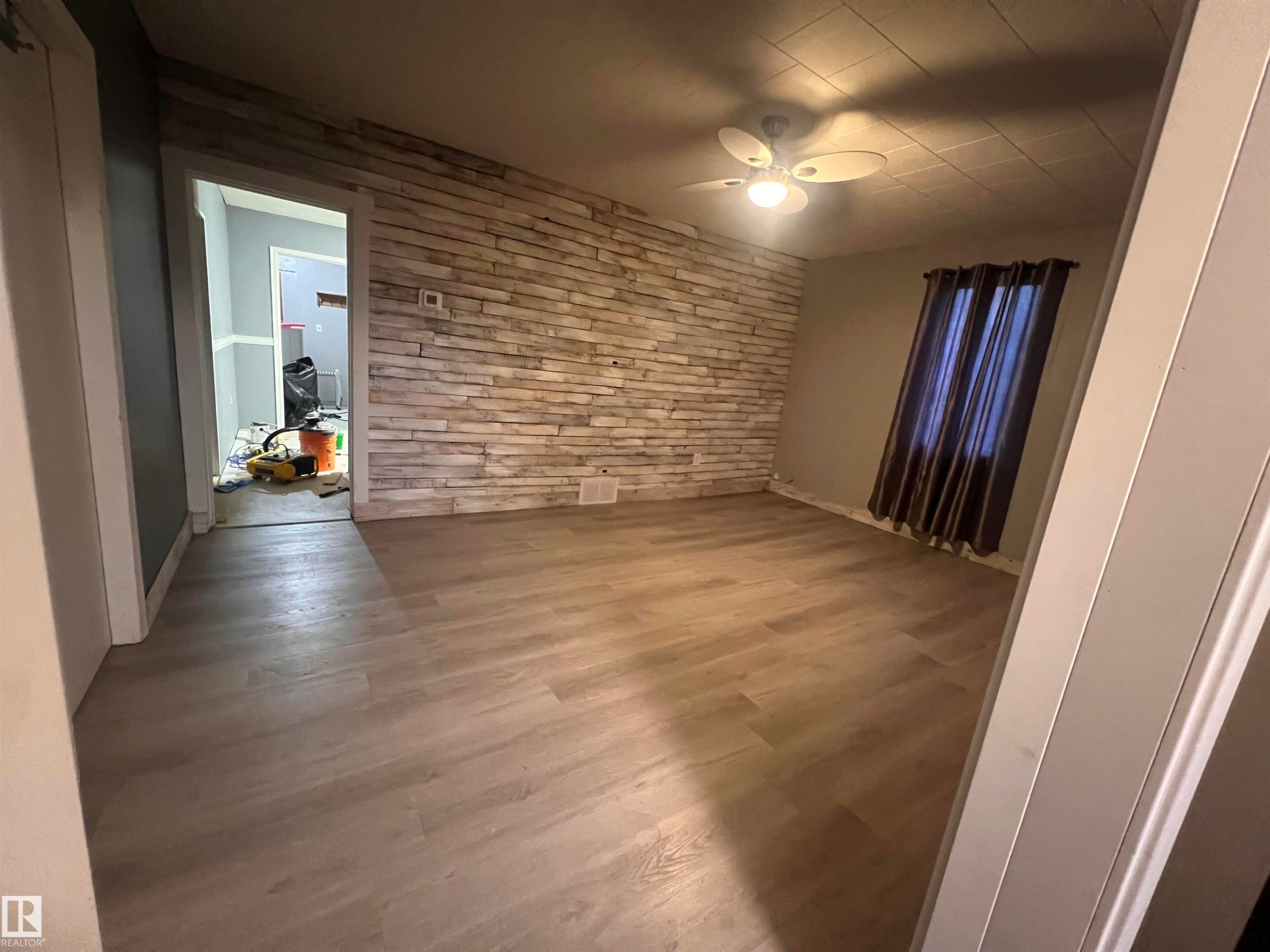 Interior room featuring a textured stone-finish accent wall, wood-finish flooring, and a ceiling fan with integrated lighting - 69 Railway Avenue, Star, AB