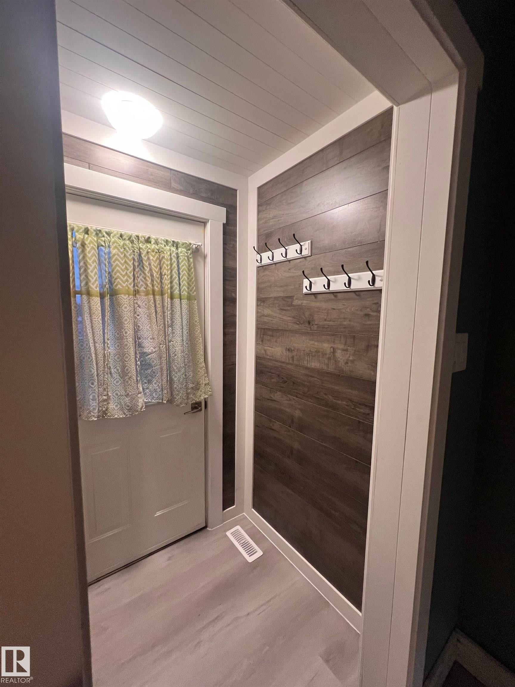 Entryway featuring light wood-finish flooring, dark wood-finish accent wall, and a white planked ceiling - 69 Railway Avenue, Star, AB