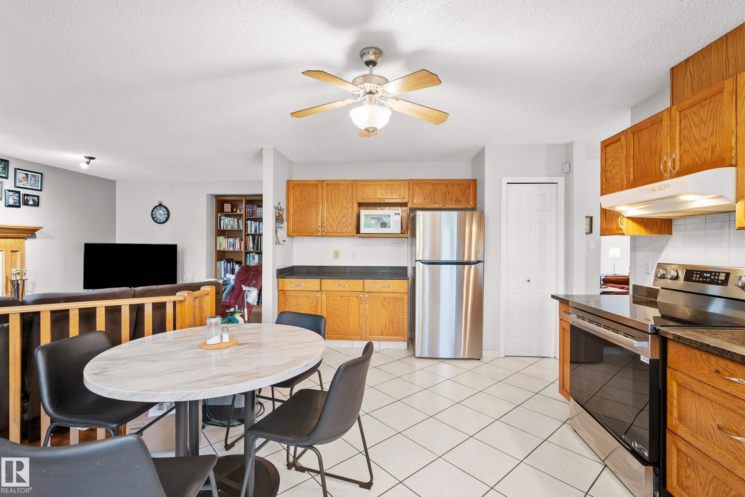 Kitchen featuring tile flooring, wood cabinetry, stainless steel refrigerator, and stainless steel range - 15503 62 Street, Edmonton, AB
