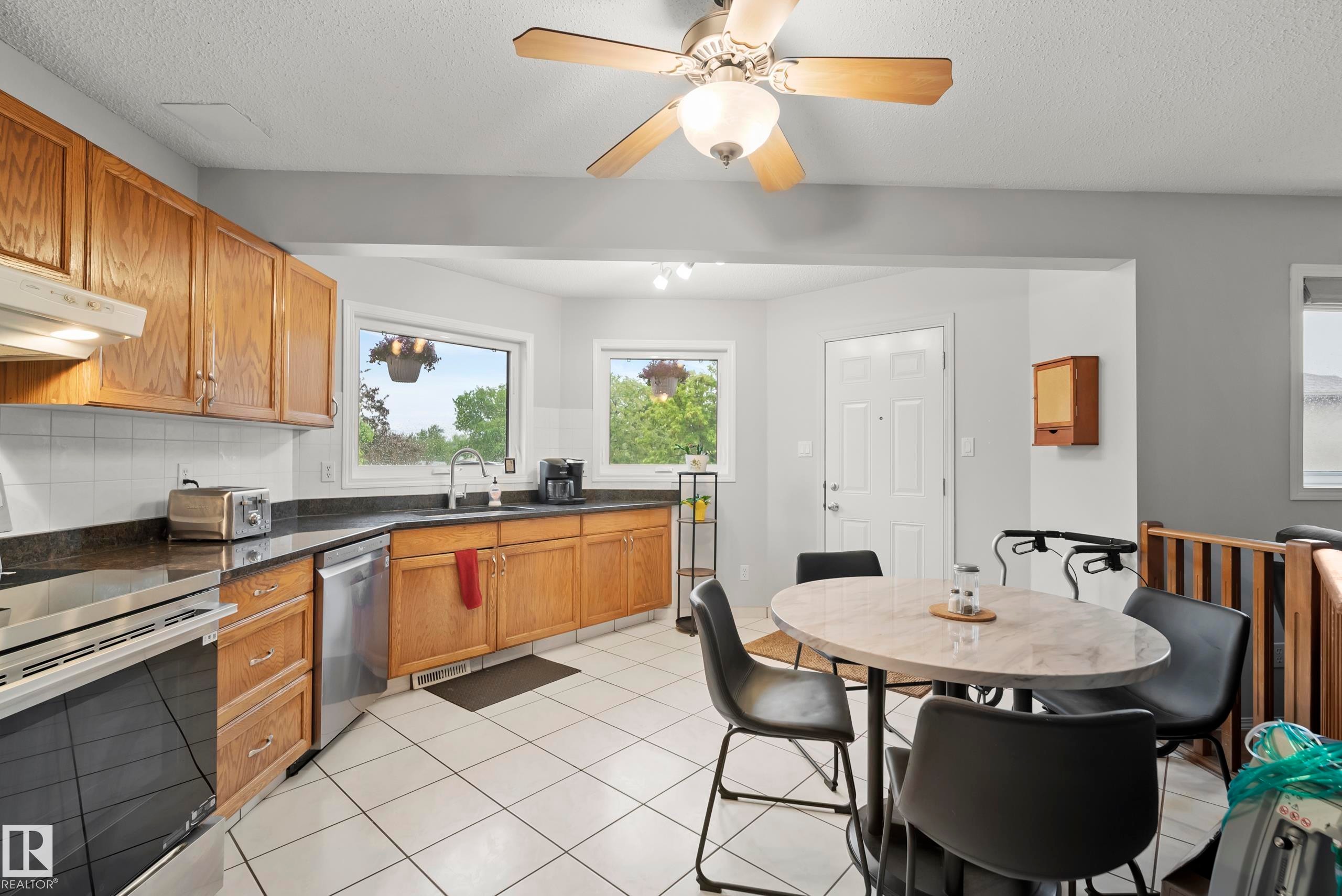 Kitchen featuring wood cabinetry, dark countertops, white tile backsplash, and stainless steel appliances including a range and dishwasher - 15503 62 Street, Edmonton, AB