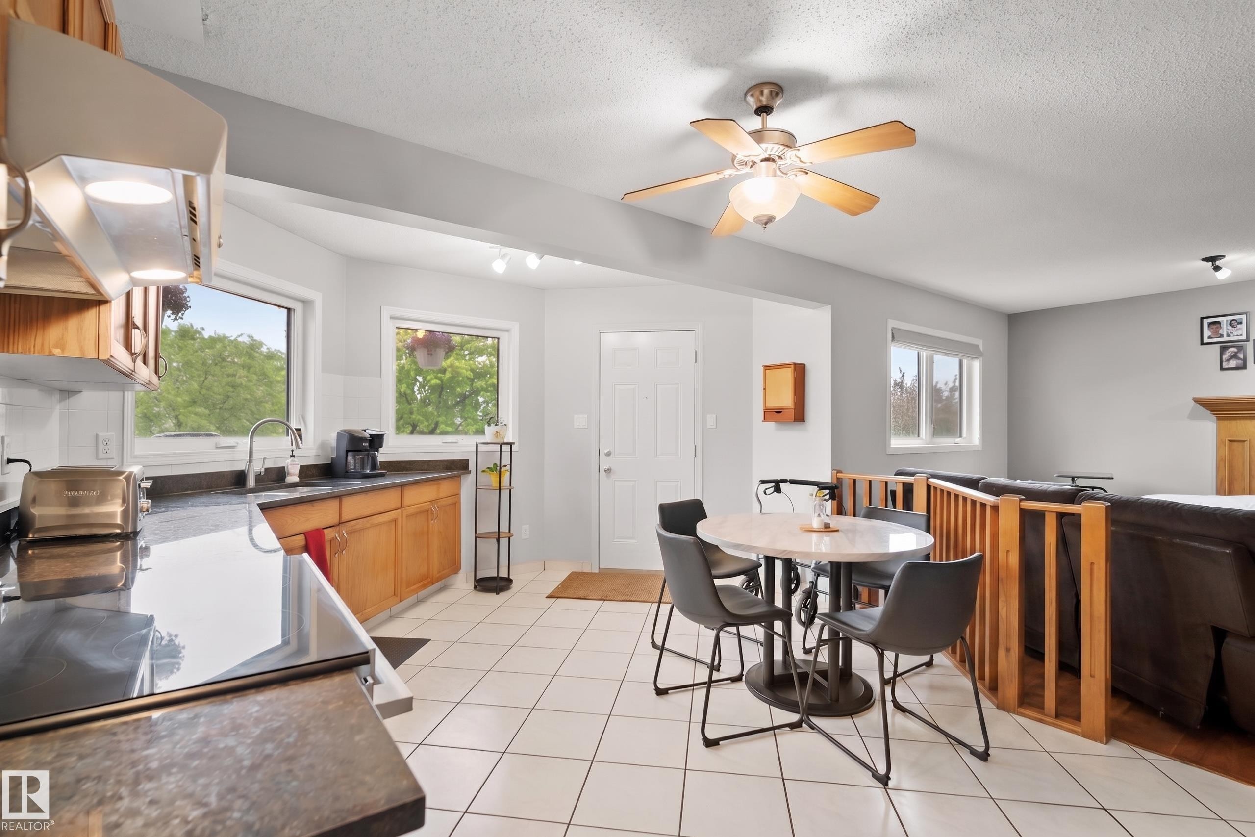 Open-concept kitchen and dining area featuring light wood cabinetry, dark countertops, white tile flooring, and a ceiling fan - 15503 62 Street, Edmonton, AB