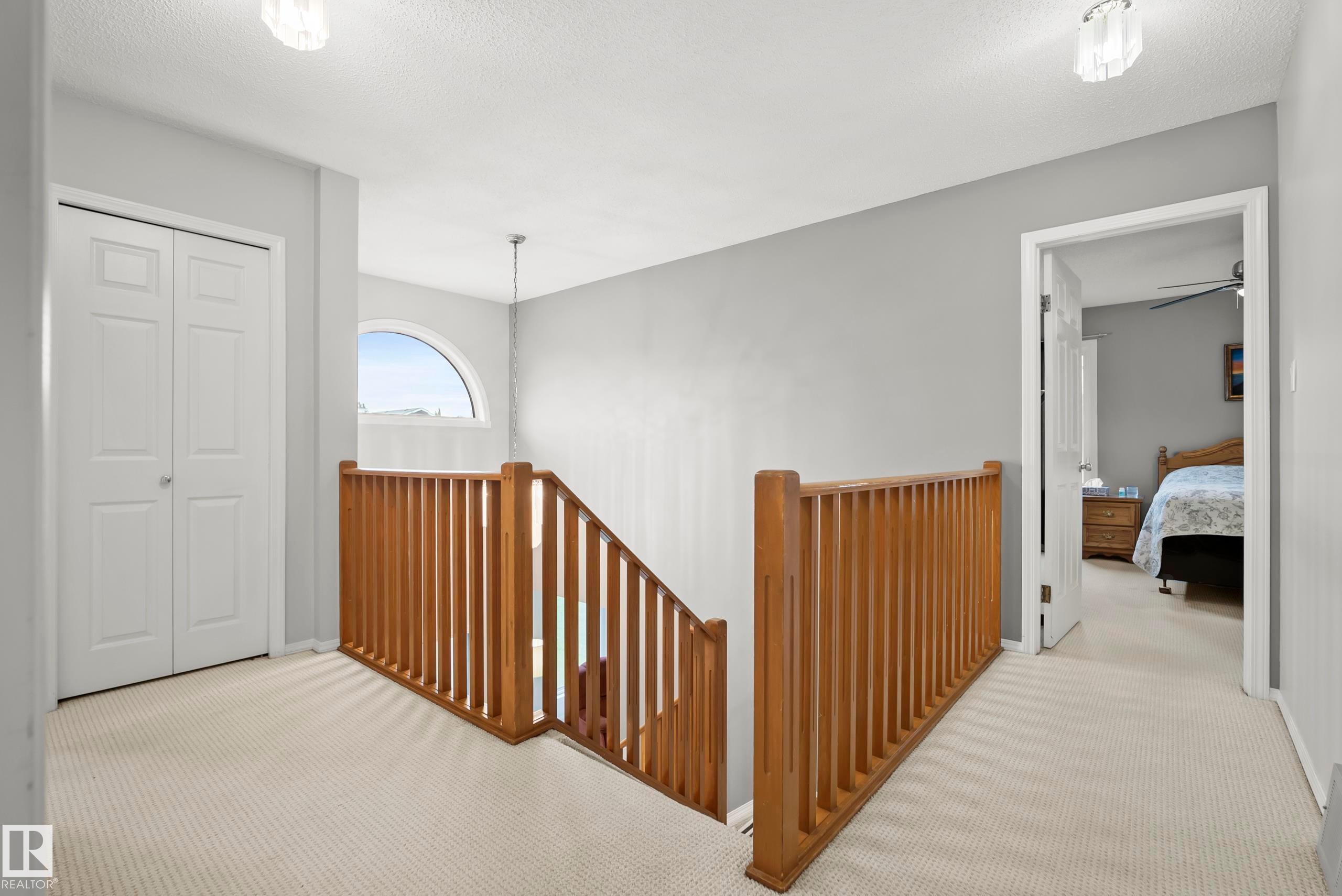 Upper level landing featuring light-toned carpeting, a wood railing, and an arched window - 15503 62 Street, Edmonton, AB