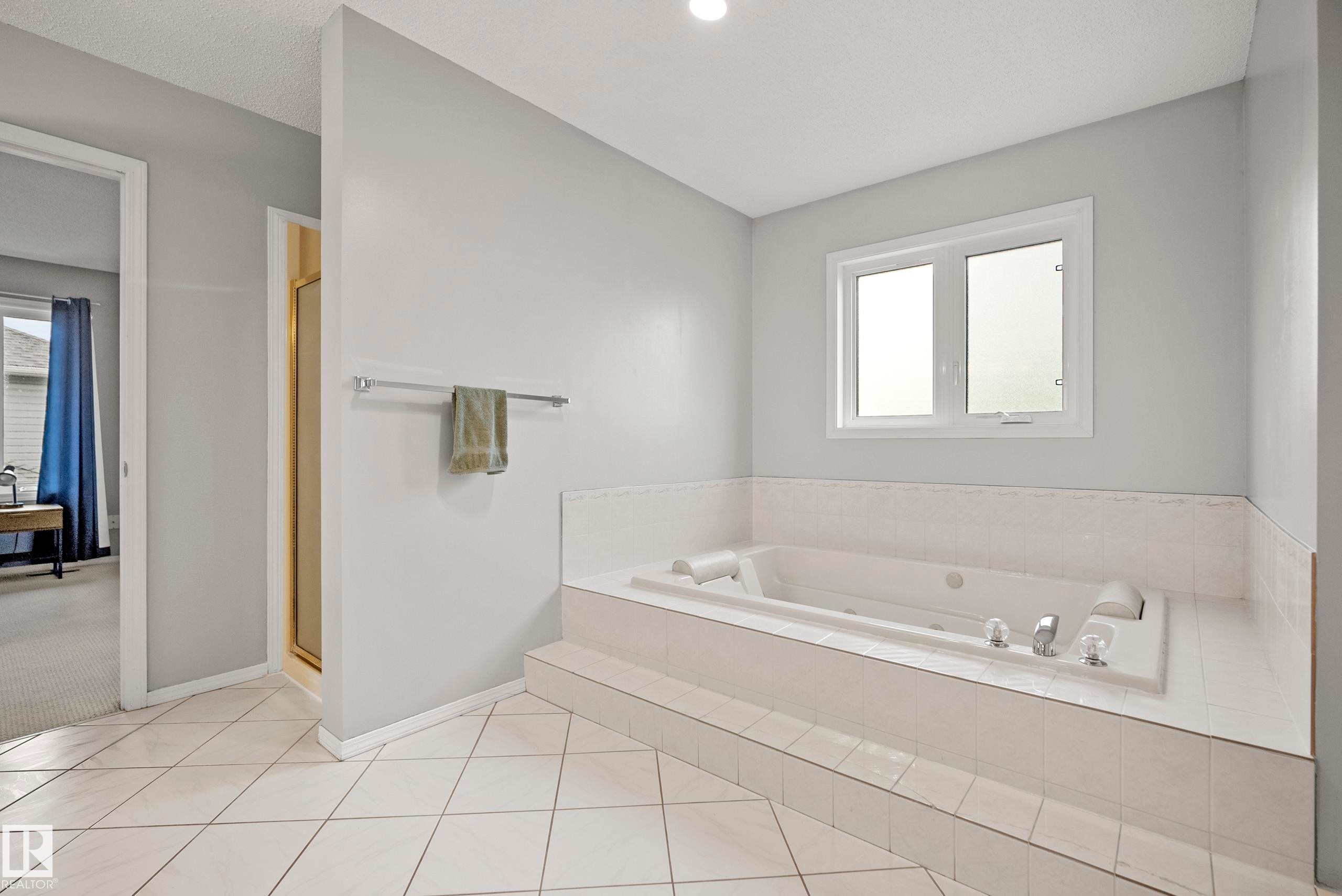 Soaking tub with tiled surround, single window, chrome fixtures, and a white tiled floor - 15503 62 Street, Edmonton, AB