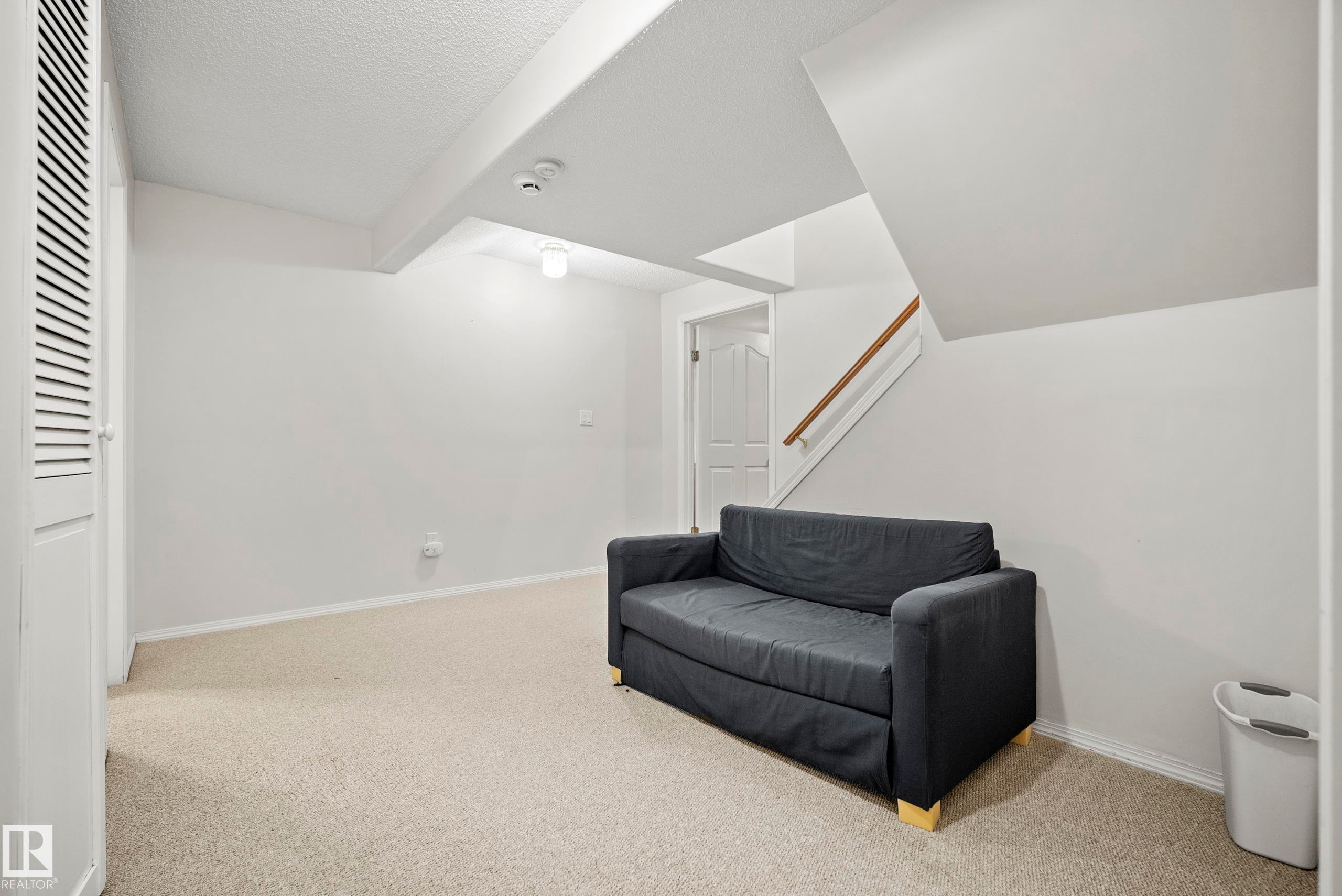 Carpeted room featuring a louvered bi-fold door, a paneled interior door, and a staircase with a wood-finish handrail - 15503 62 Street, Edmonton, AB