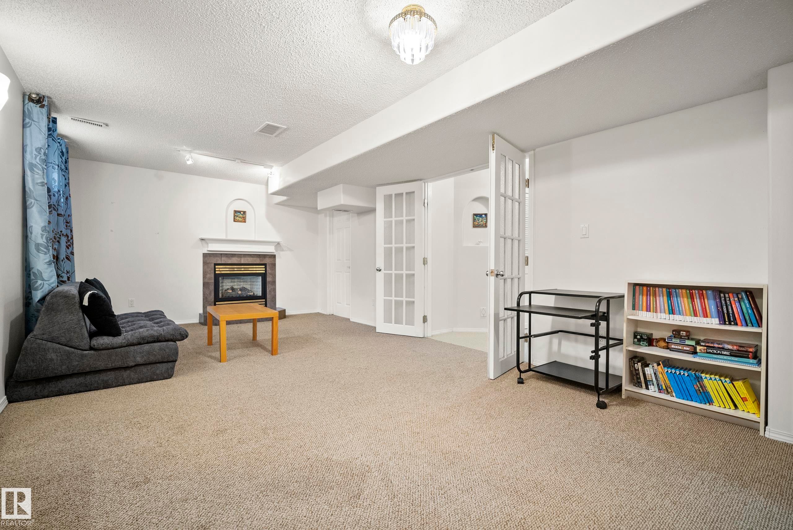 Carpeted room featuring a fireplace with a stone-tile surround, white mantel, and arched niche - 15503 62 Street, Edmonton, AB