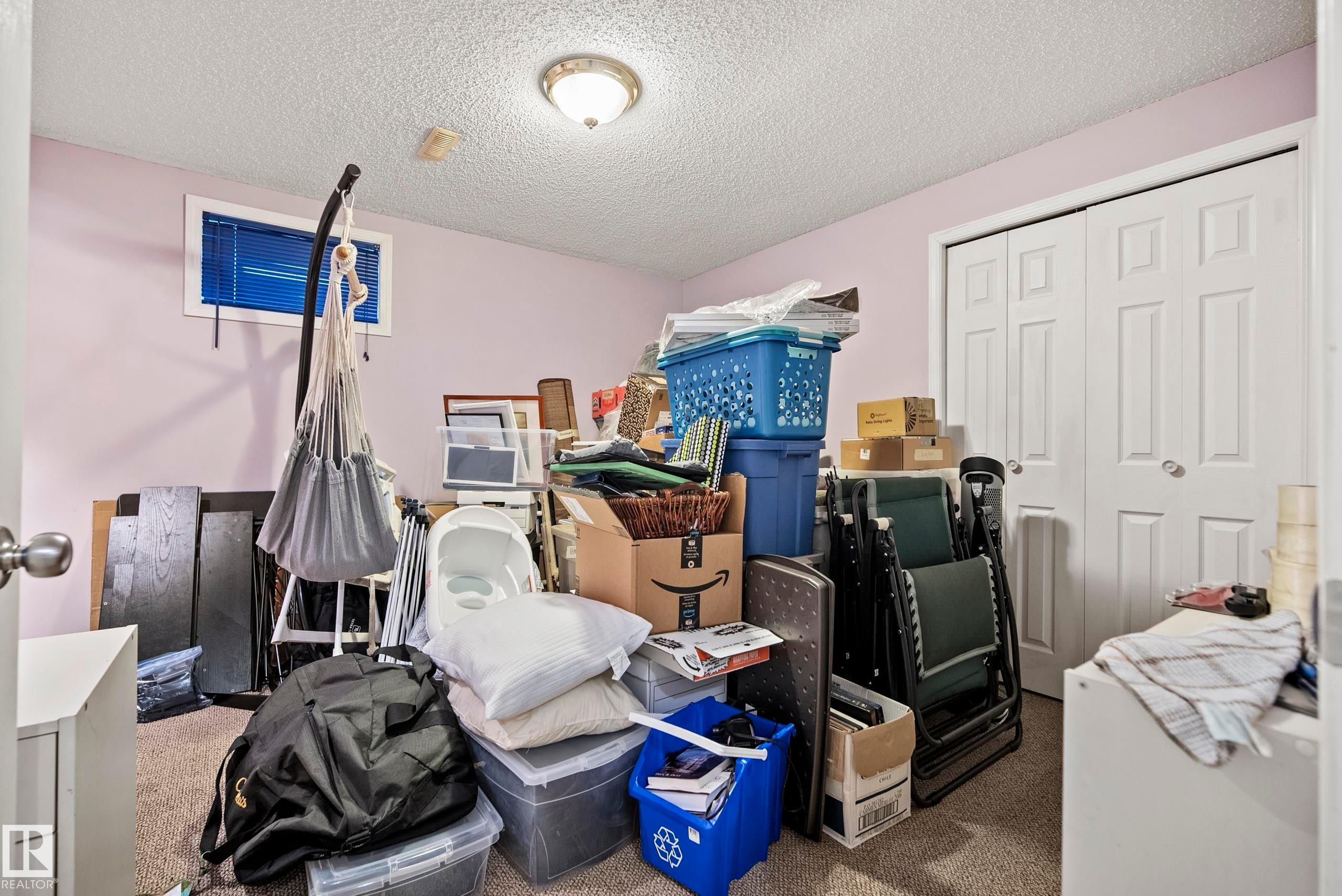 White bi-fold closet doors provide storage solutions within this room featuring a window with blue blinds, a flush mount ceiling light fixture, and textured ceiling - 15503 62 Street, Edmonton, AB