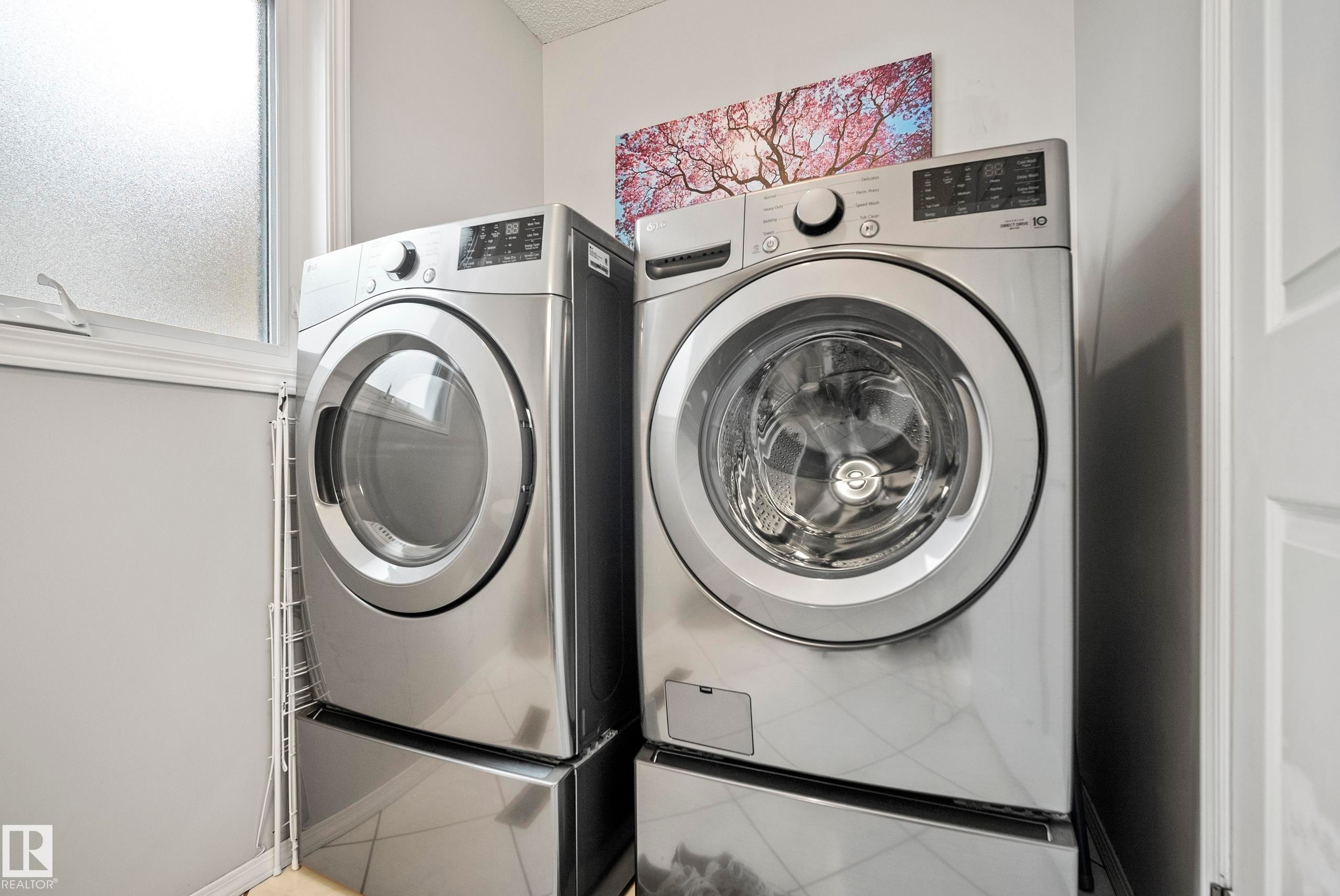 Dedicated laundry area featuring a front-loading washer and dryer, both in a stainless steel finish, set upon coordinating pedestals - 15503 62 Street, Edmonton, AB