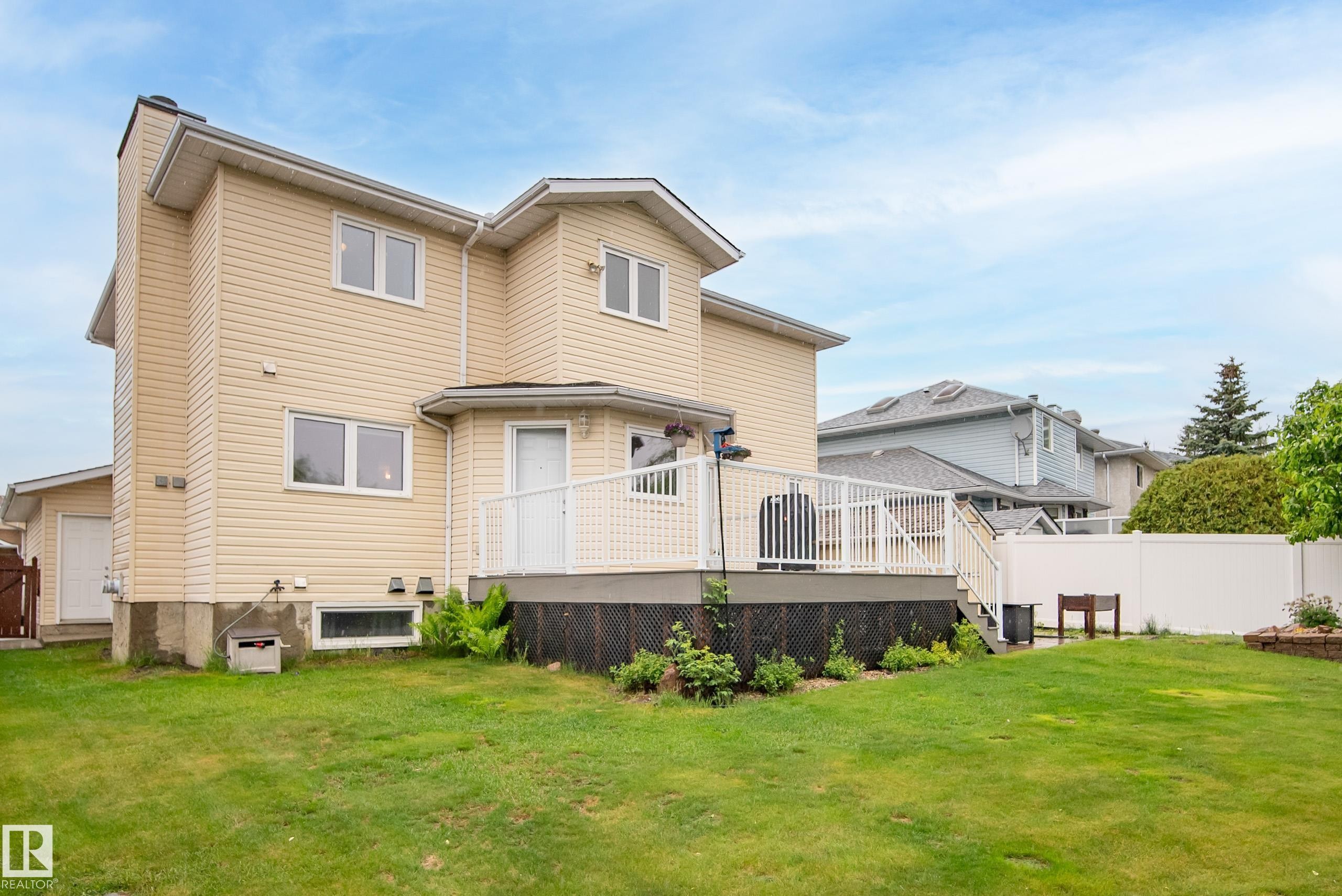 Rear exterior featuring a multi-level deck with white railings, a detached garage, and a spacious lawn - 15503 62 Street, Edmonton, AB