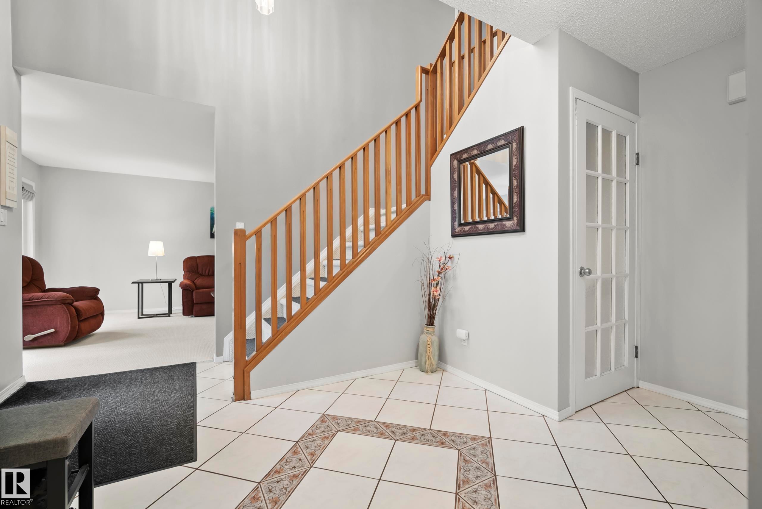 Entryway featuring a natural wood staircase, white tile flooring with decorative inlay, and a multi-pane interior door - 15503 62 Street, Edmonton, AB