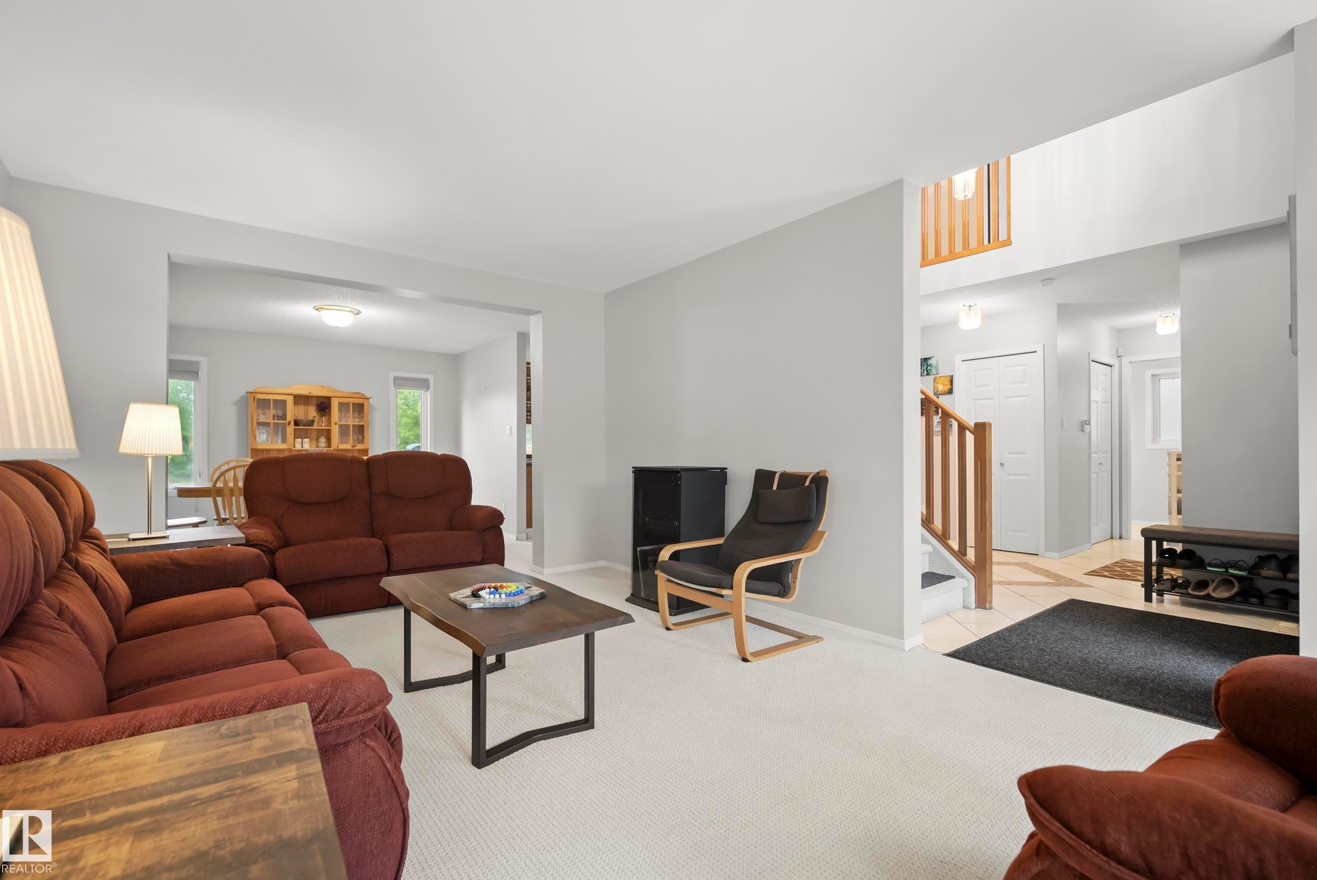 Living area featuring light gray wall paint, carpeting, and an entryway with wood-finish railing and tiled flooring - 15503 62 Street, Edmonton, AB