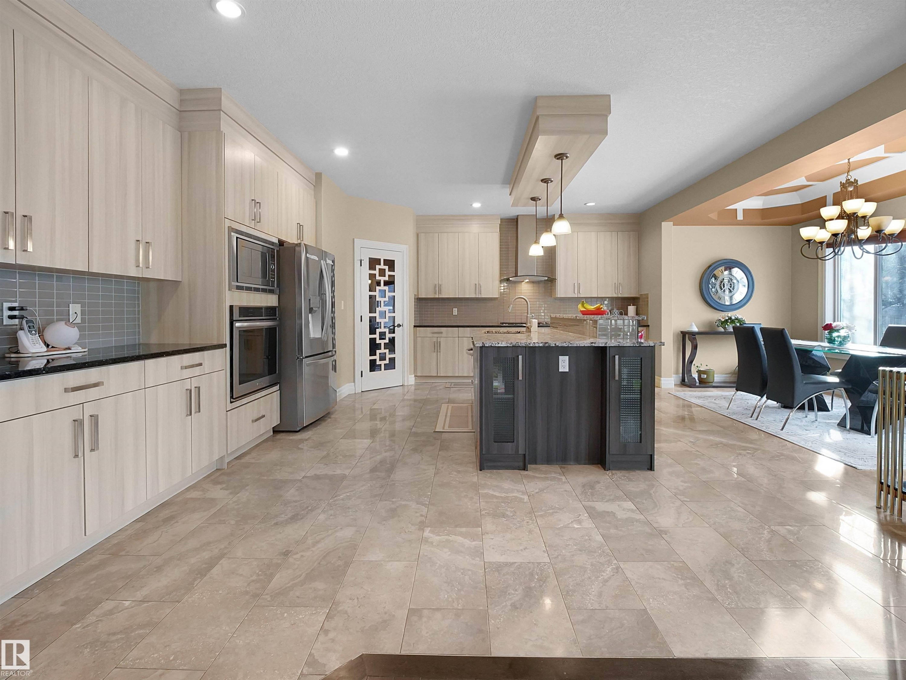 Spacious kitchen featuring light-toned cabinetry, stainless steel appliances, dark countertops, a contrasting central island, pendant lighting and large format tile flooring - 2019 Cameron Ravine Way Nw, Edmonton, AB