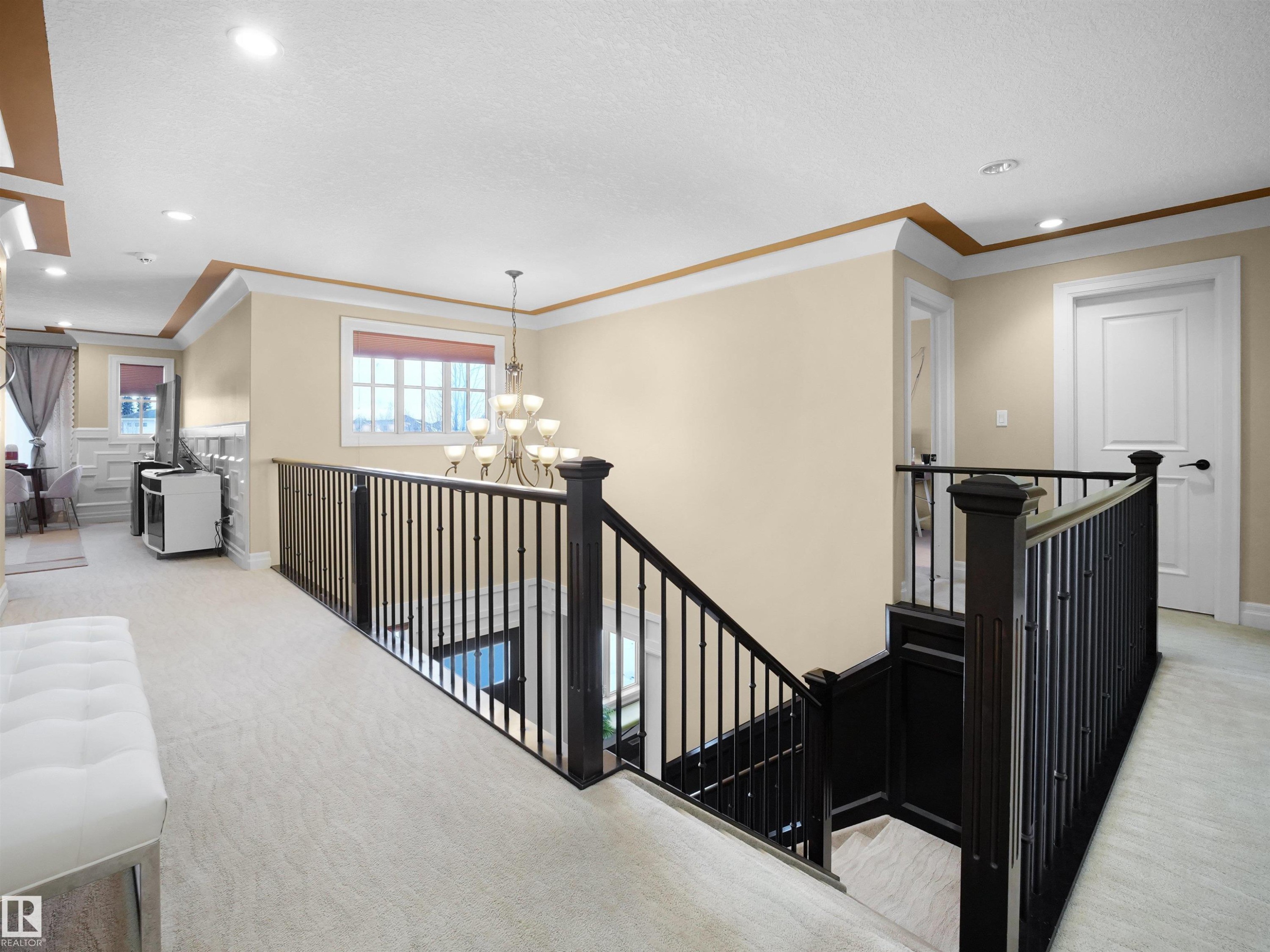 Upper-level landing featuring light-toned carpeting, dark wood-finish newel posts and railings, white panel doors, recessed lighting, and crown molding accents - 2019 Cameron Ravine Way Nw, Edmonton, AB