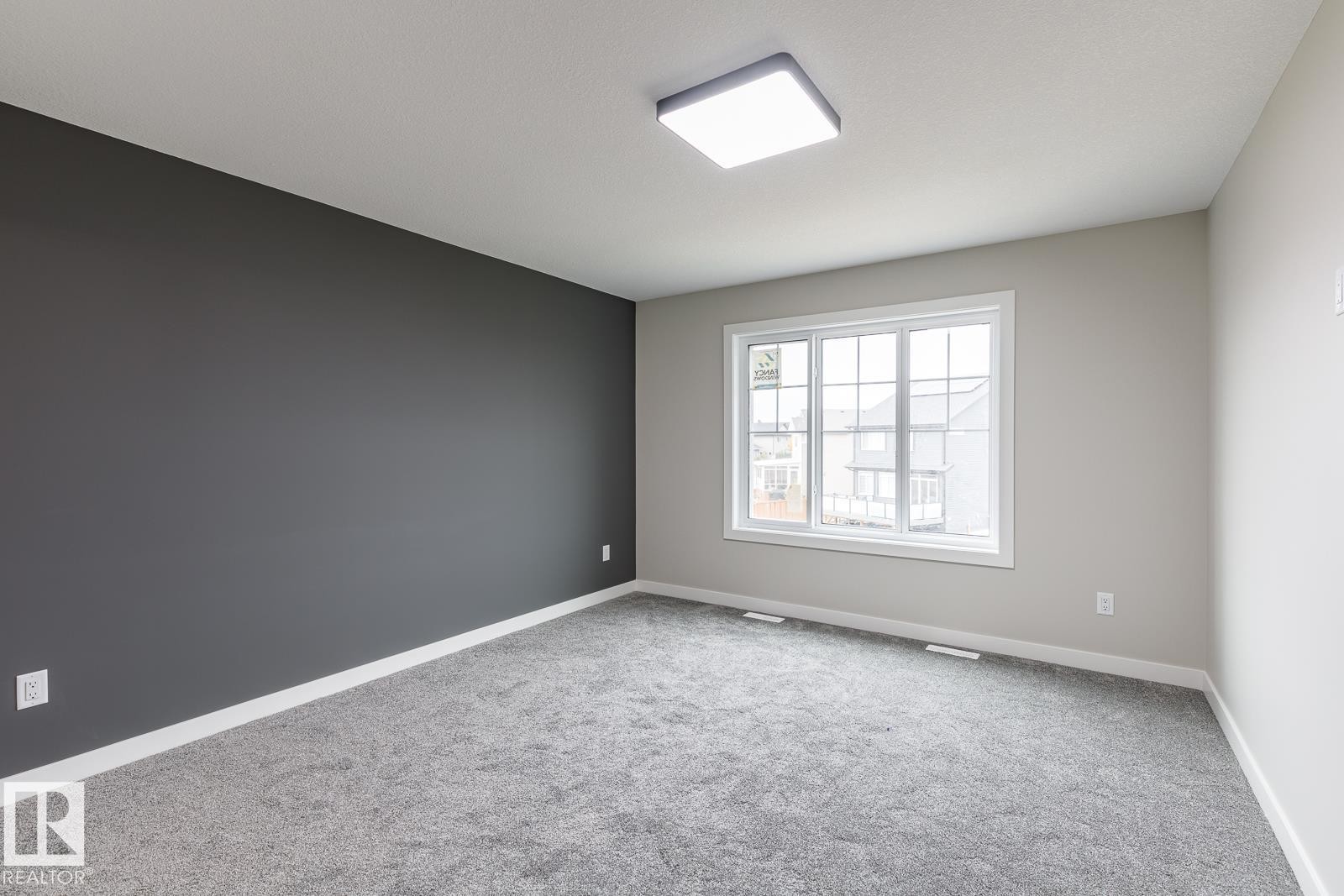 Carpeted interior space featuring a large window with white trim, a dark accent wall, and a square flush-mount ceiling light - 50 Chartres Close, St. Albert, AB