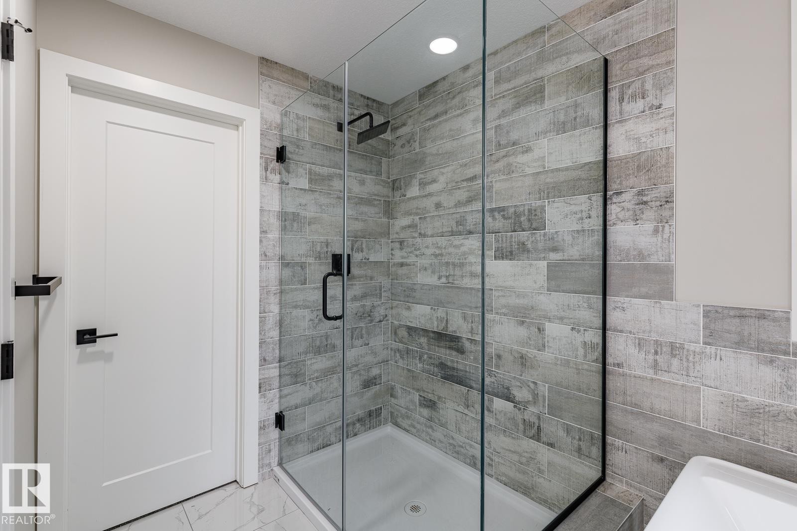 Shower enclosure featuring clear glass panels, matte black hardware, and wood-look tile surround - 50 Chartres Close, St. Albert, AB