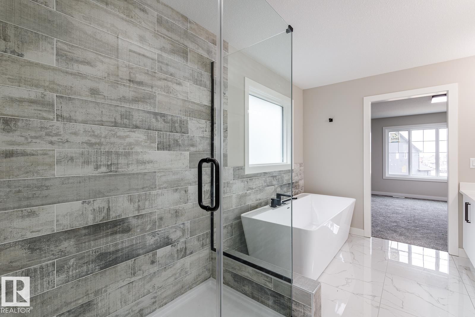 Modern bathroom featuring a frameless glass shower enclosure with wood-look tile, a freestanding soaking tub with matte black fixtures, and polished marble-look floor tiles - 50 Chartres Close, St. Albert, AB