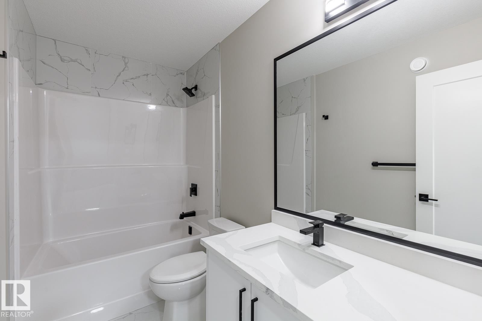 Bathroom featuring a white bathtub and shower surround with a marble-patterned accent tile band - 50 Chartres Close, St. Albert, AB